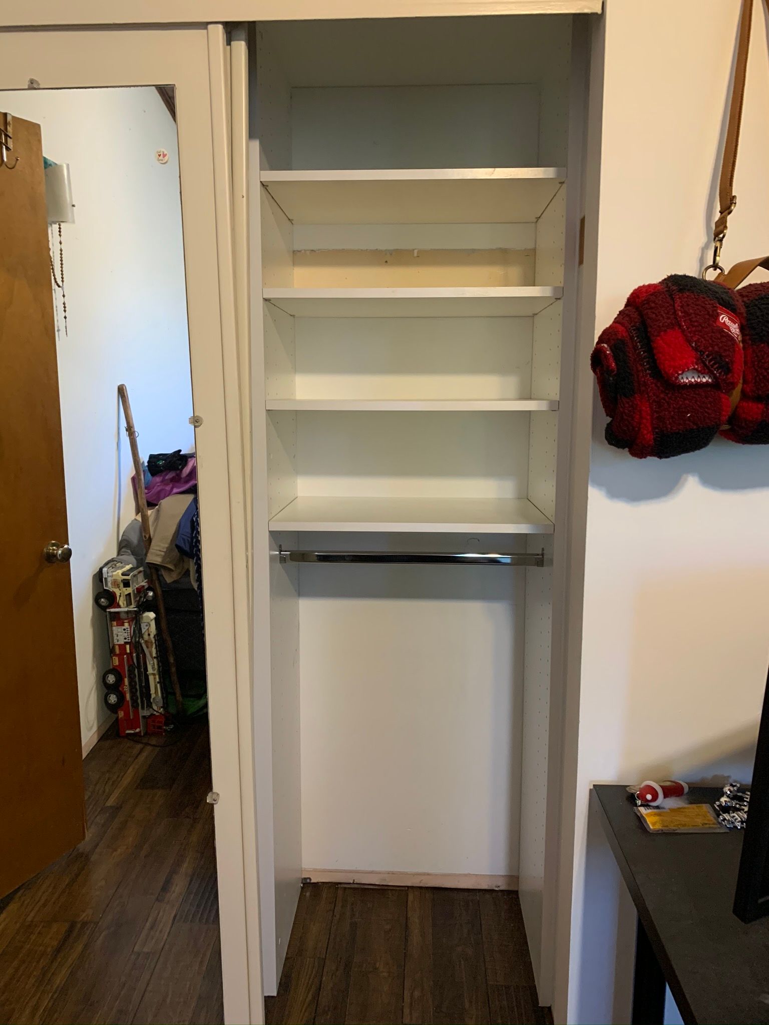 White closet interior with shelves and a hanging rod. Doorway and items visible.