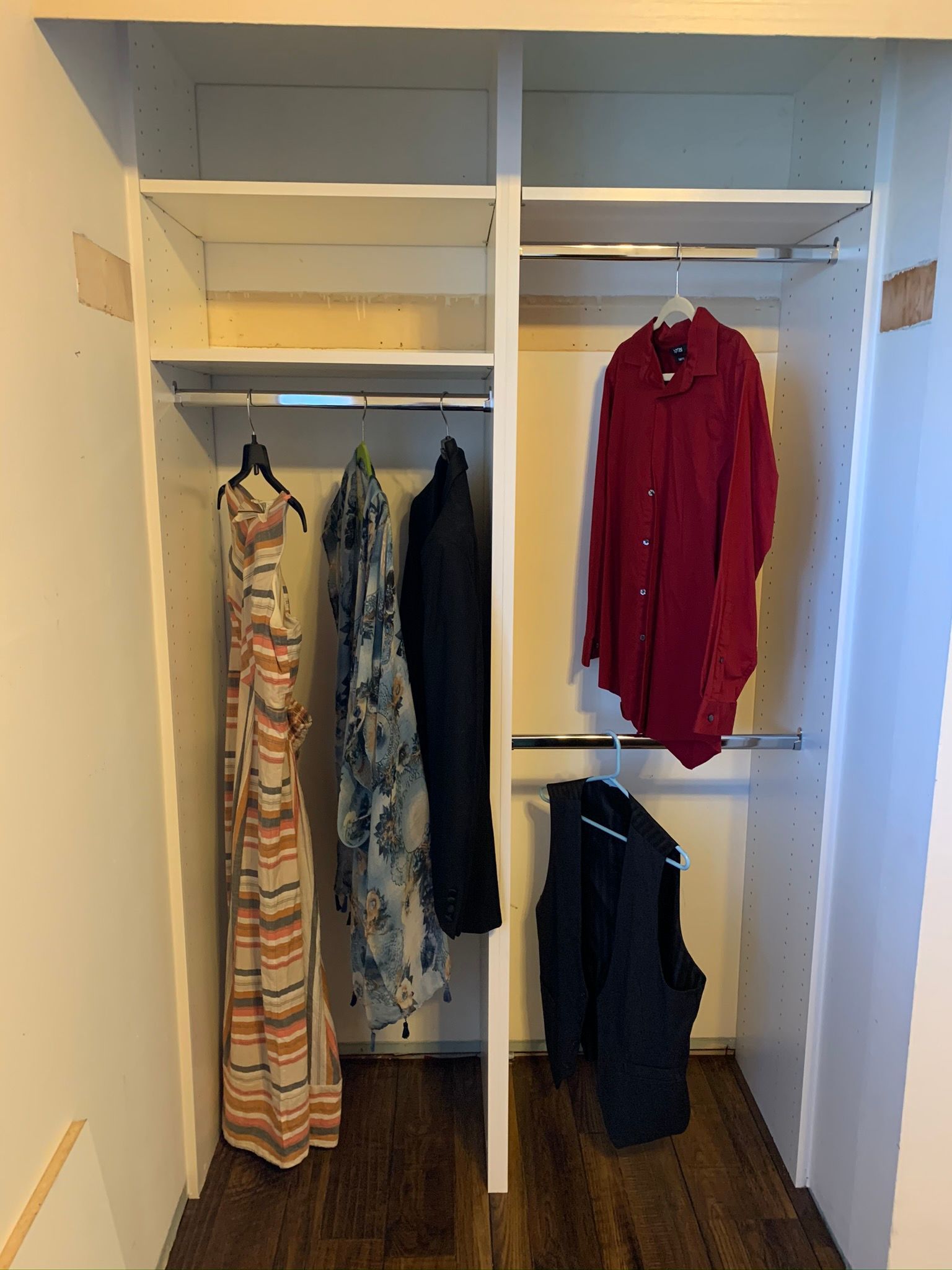 White closet with clothes hanging: dresses, shirt, and vest. Dark wood floor.