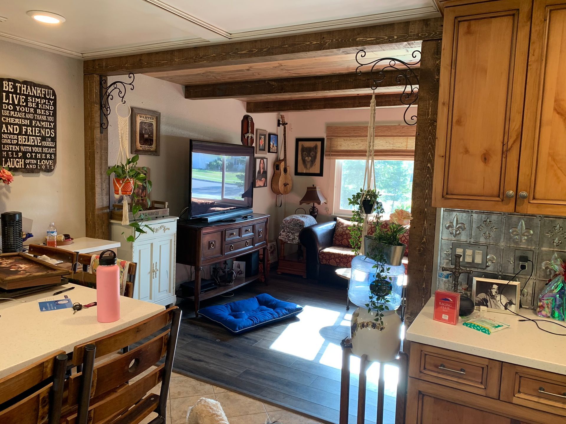 Kitchen with view into living room, featuring a TV, wood beams, and a window.