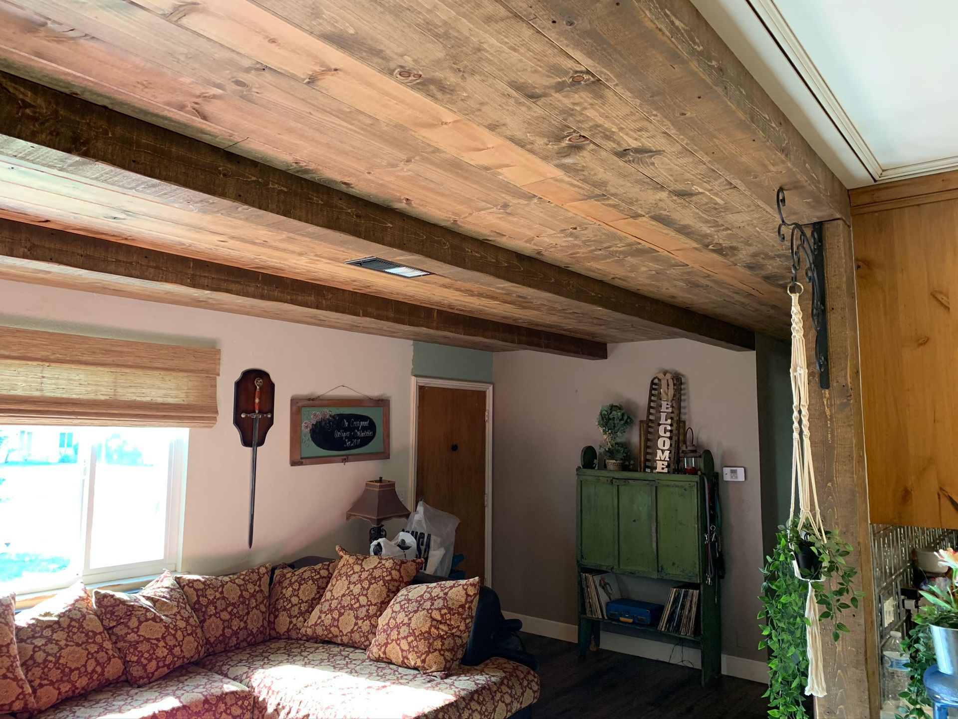 Living room with rustic wood ceiling beams, couch, green cabinet, and window with blinds.