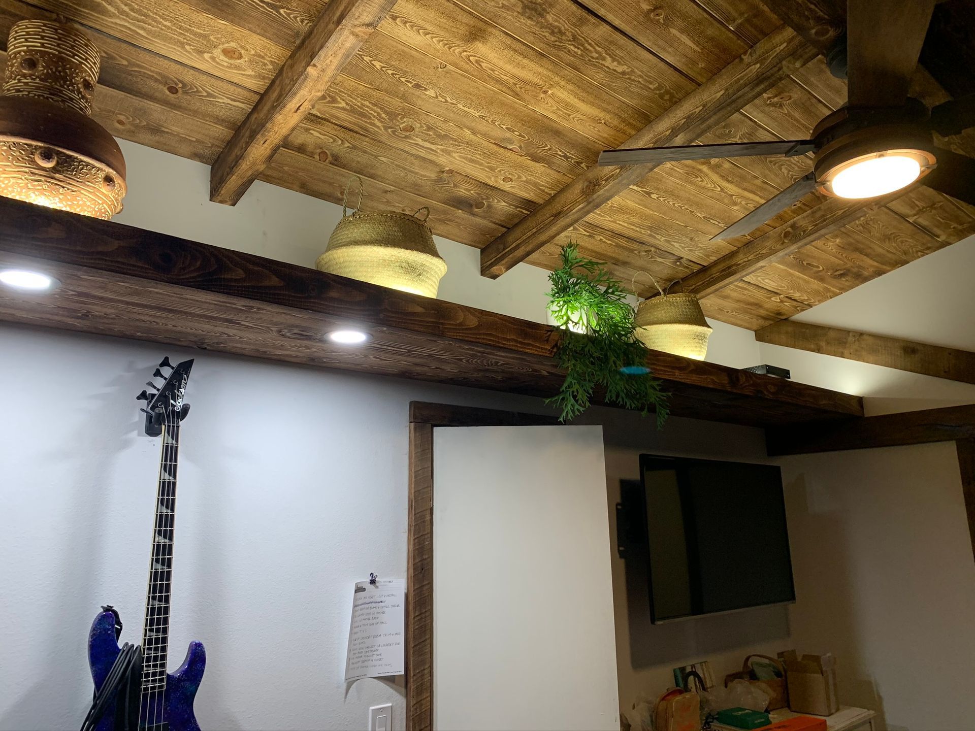 Wooden ceiling with beams and lights, an electric guitar, a TV, and decorative baskets.