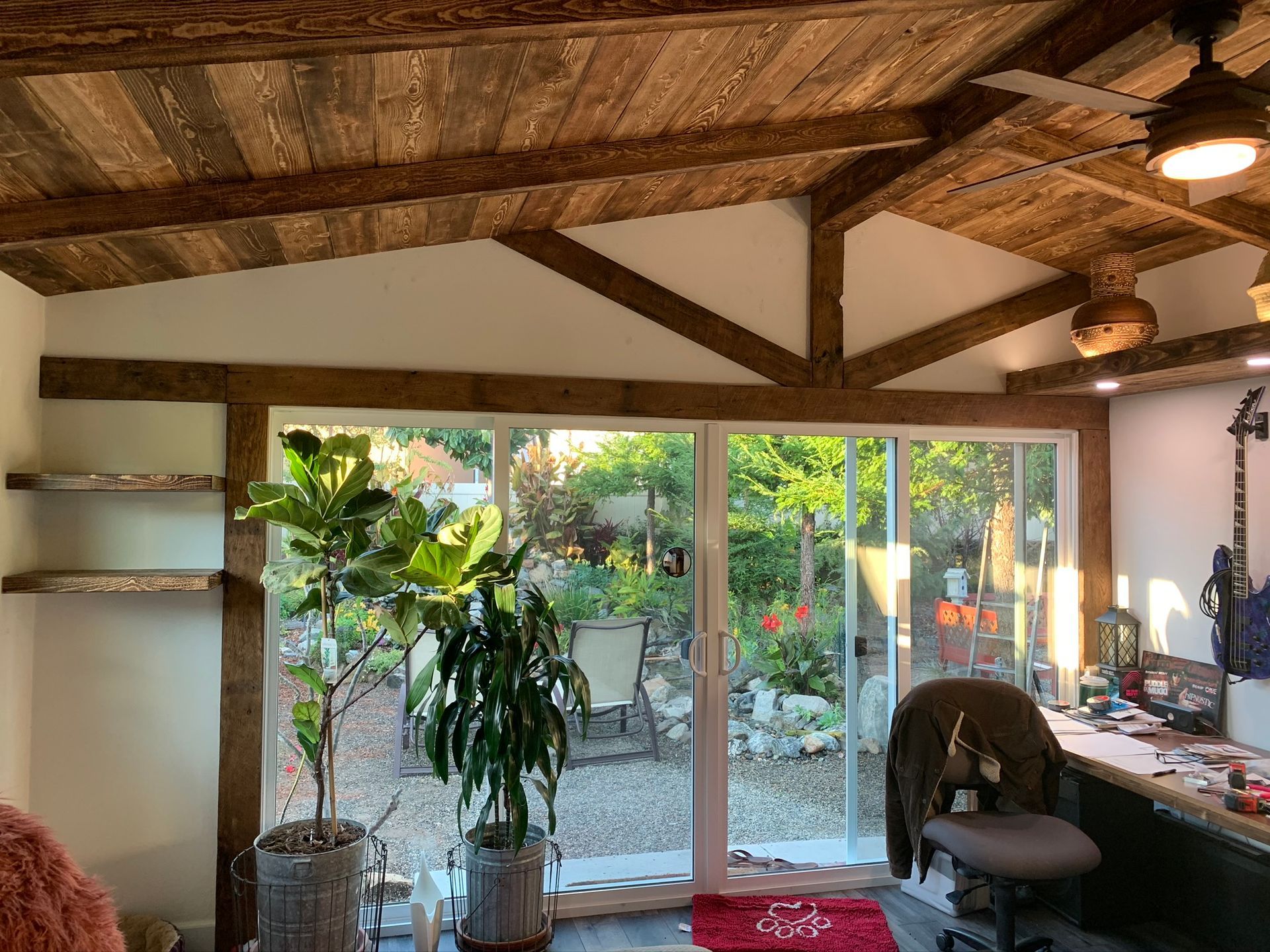 Room with wood beams, sliding glass doors, plants, and a view of a garden.