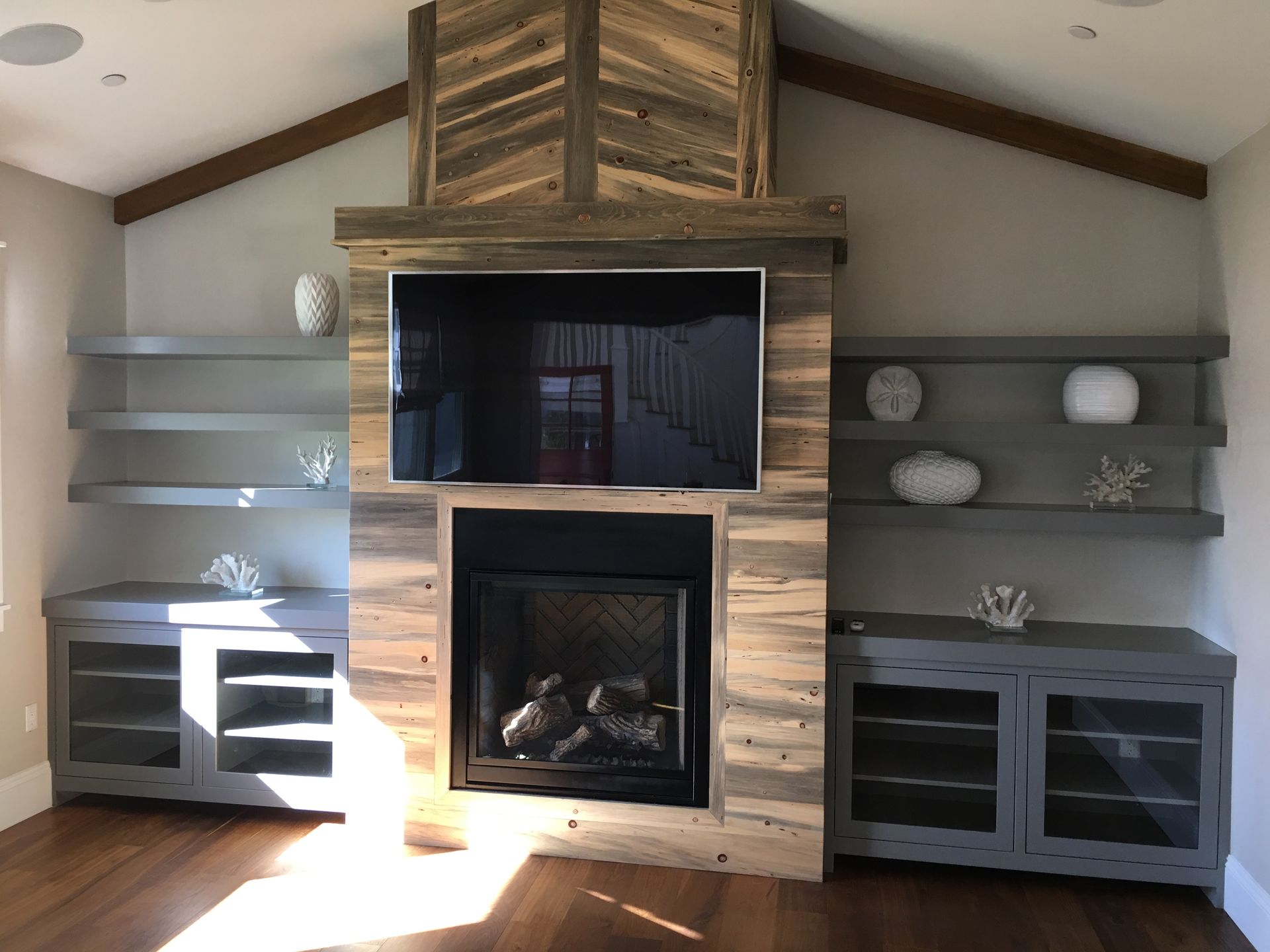 Fireplace with rustic wood and built-in gray shelving and cabinets. TV above the fireplace.
