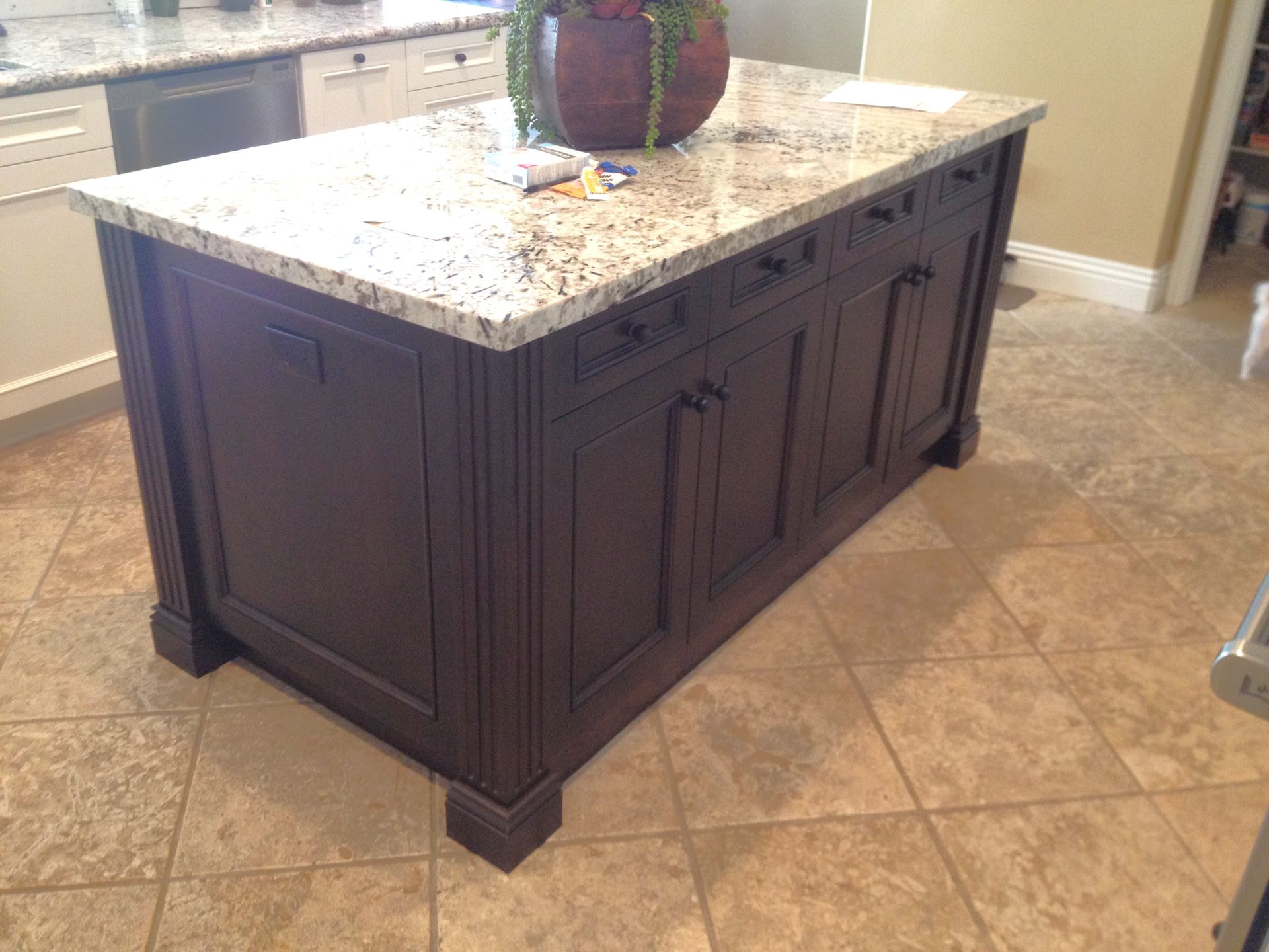 Dark wooden kitchen island with granite countertop. Brown tile floor.