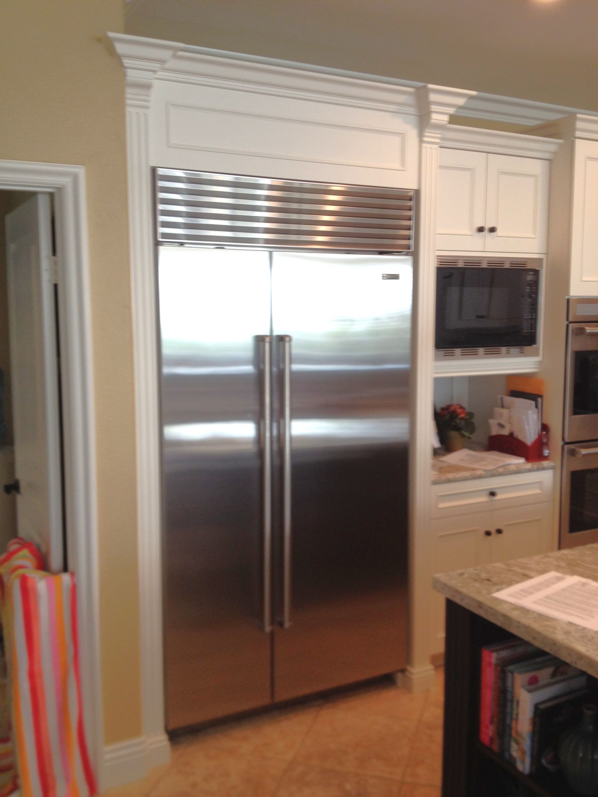 Stainless steel refrigerator built into white cabinetry in a kitchen, with a microwave and cabinets nearby.