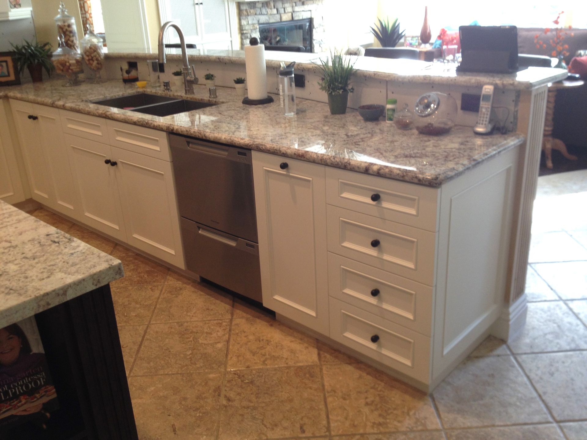 White kitchen island with granite countertop, stainless steel dishwasher, drawers, and sink.