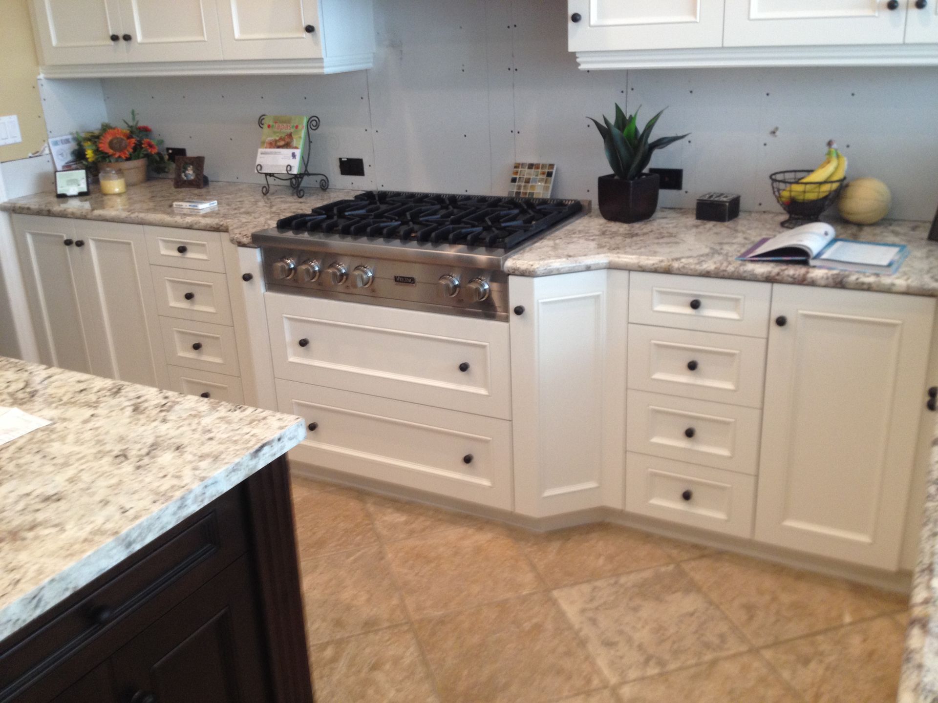 White kitchen cabinets with granite countertops surrounding a stainless steel stove on a beige tile floor.