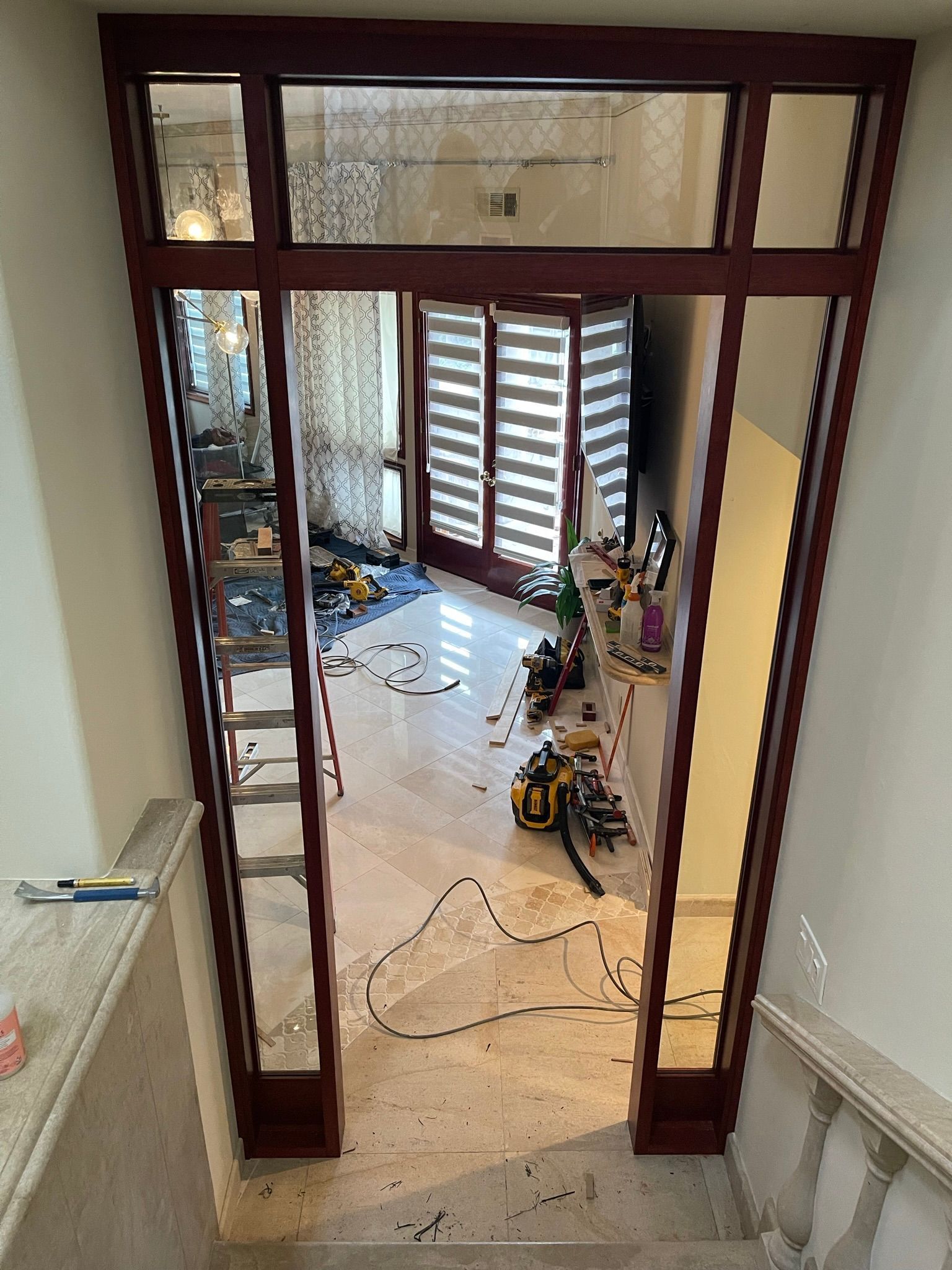 View from above: red door frame with glass panels. A room with tools and a doorway with blinds is visible beyond.