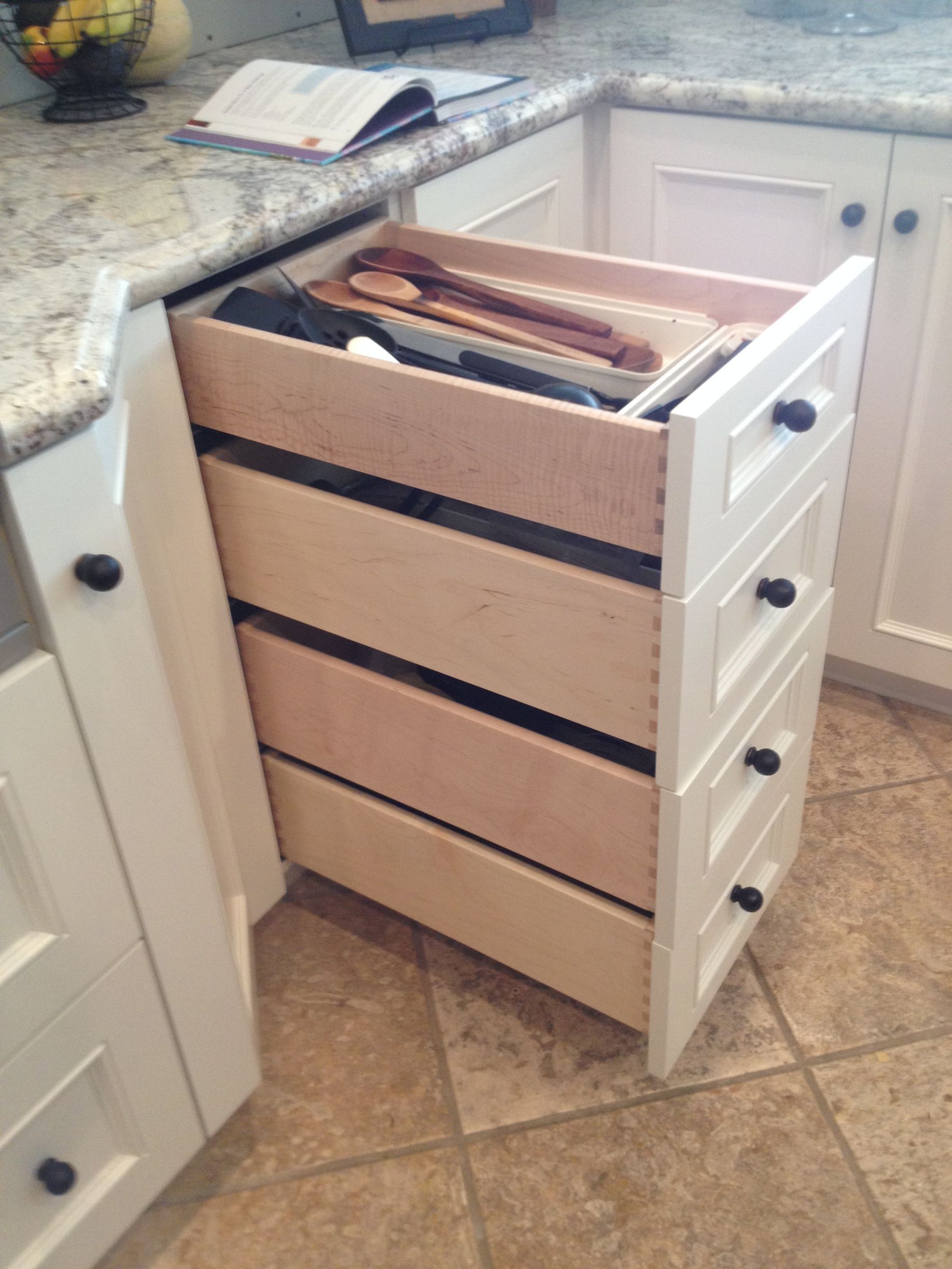 White kitchen cabinet with pull-out drawers, containing wooden utensils and other items.