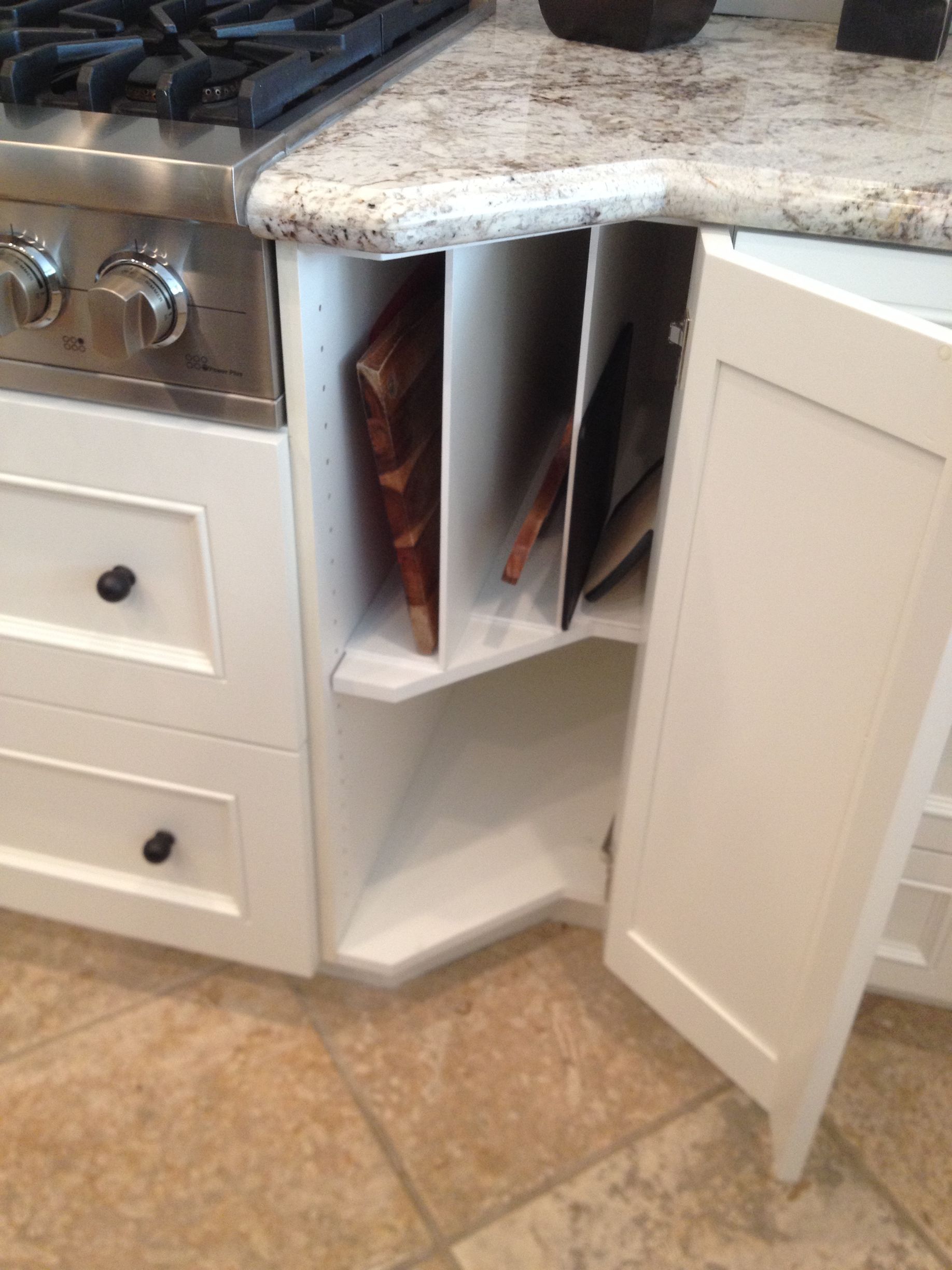 White kitchen cabinet with built-in dividers holding cutting boards, next to a stove.