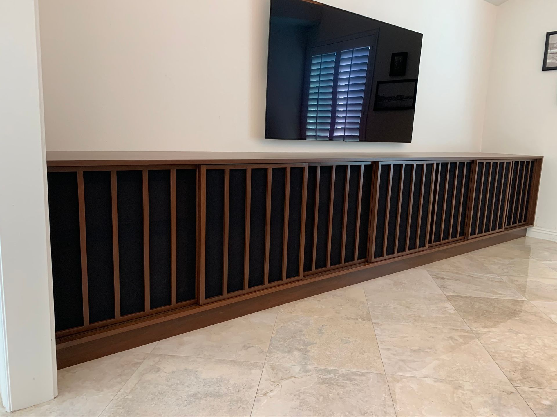 Wooden cabinet with slatted doors below a wall-mounted TV on a light-colored floor.