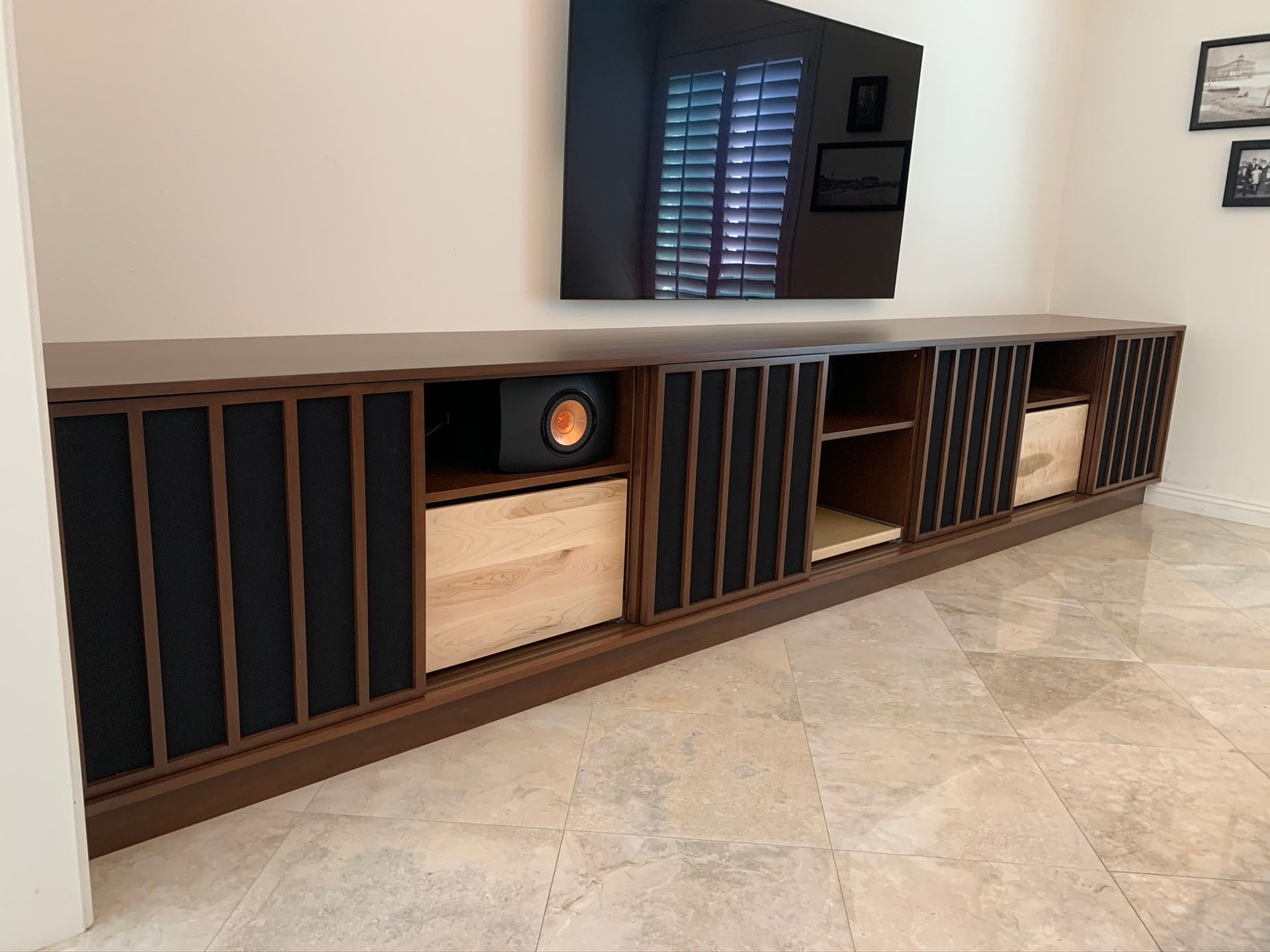 Built-in dark wood media console with a black subwoofer, drawers, and TV mounted on a white wall.