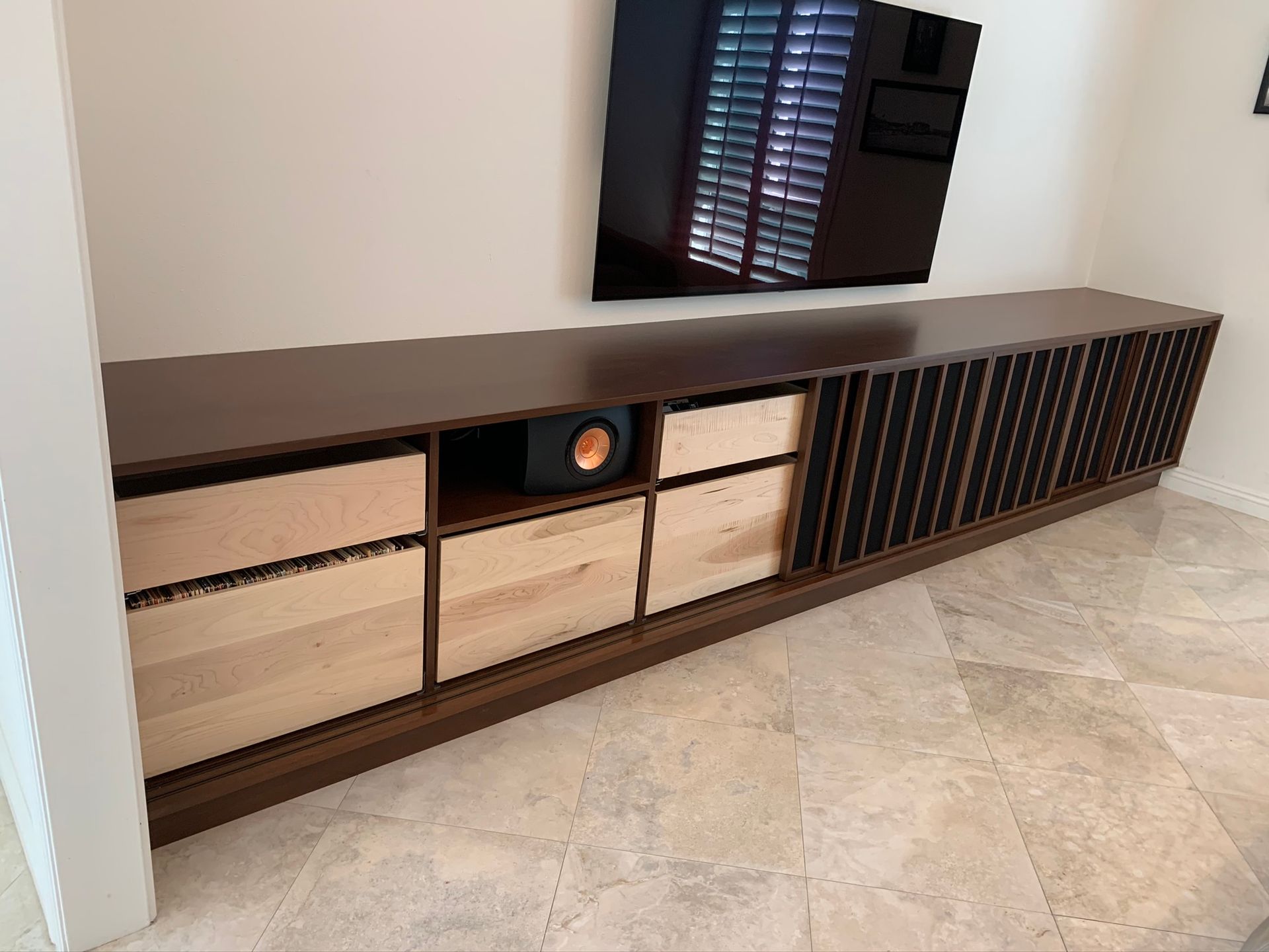 Dark wood media cabinet with drawers and speaker compartment below a wall-mounted TV.