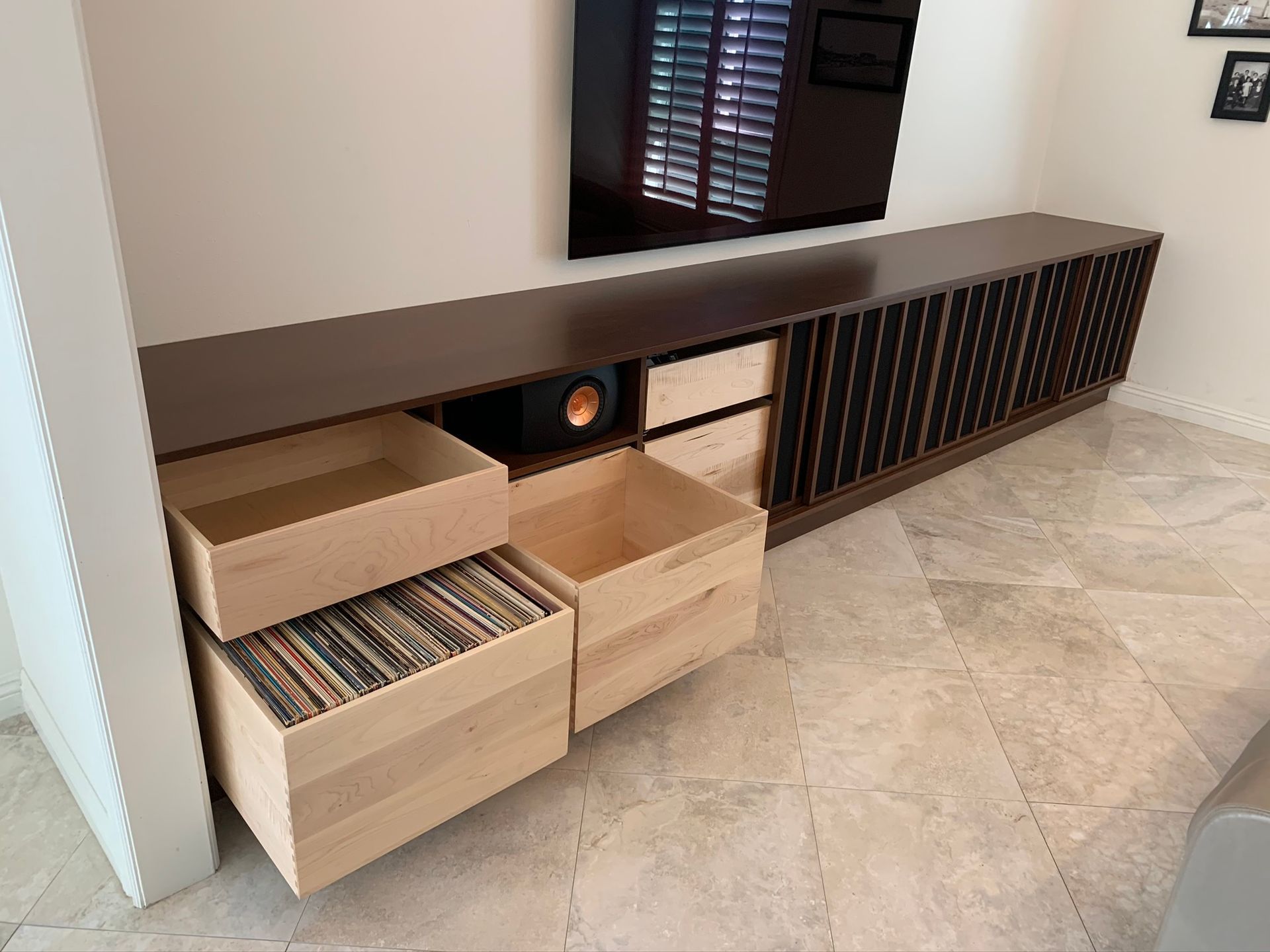 Wooden media cabinet with open drawers holding vinyl records and audio equipment, under a mounted TV.