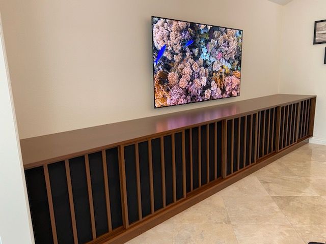 Long, low wood cabinet with vertical slats, under a mounted TV showing a colorful reef scene.