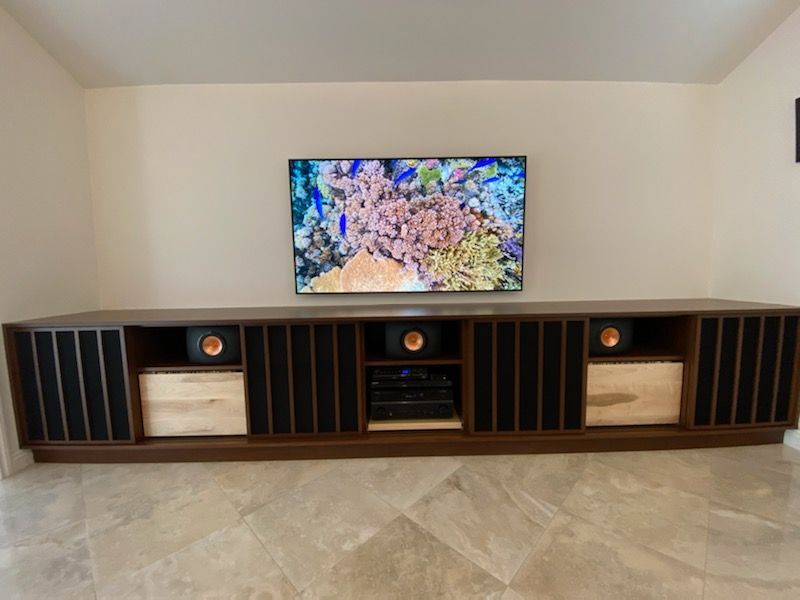 A long, dark wood entertainment center with a TV above it, featuring speakers and audio equipment.