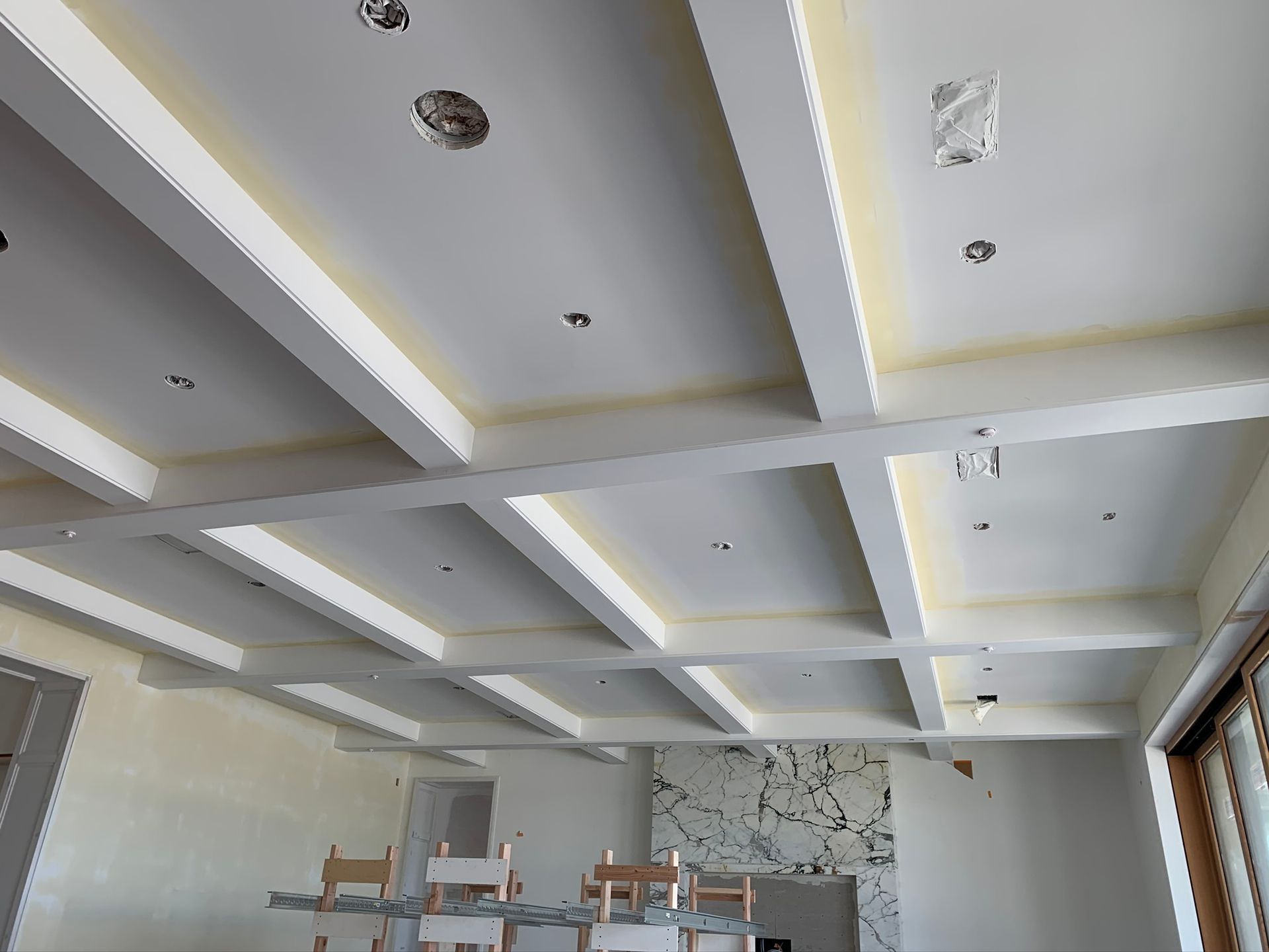 Ceiling with white beams and recessed lighting in a room under construction.