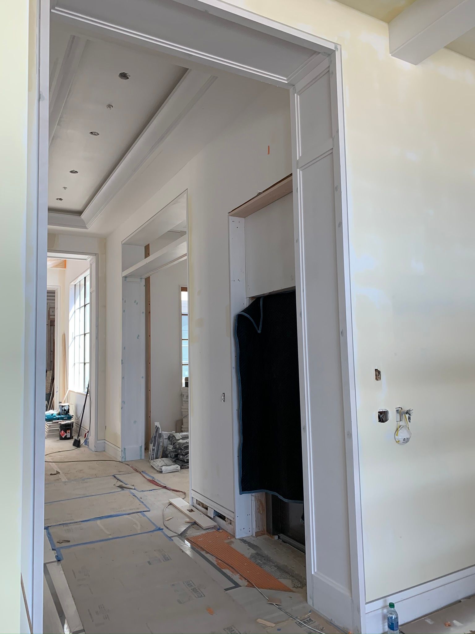 Hallway under construction with white trim, tan walls, and exposed wiring.