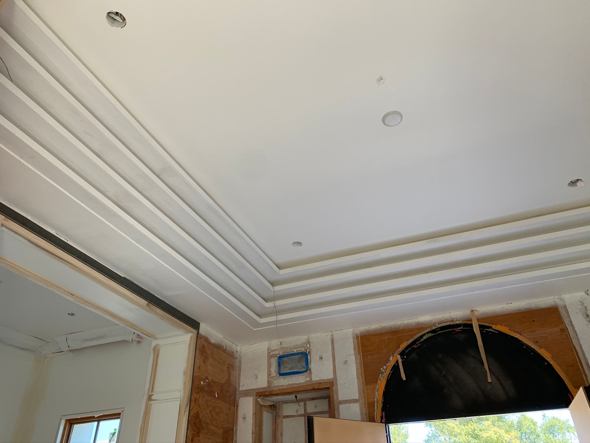 White ceiling with tiered molding and recessed lighting in a room under construction.
