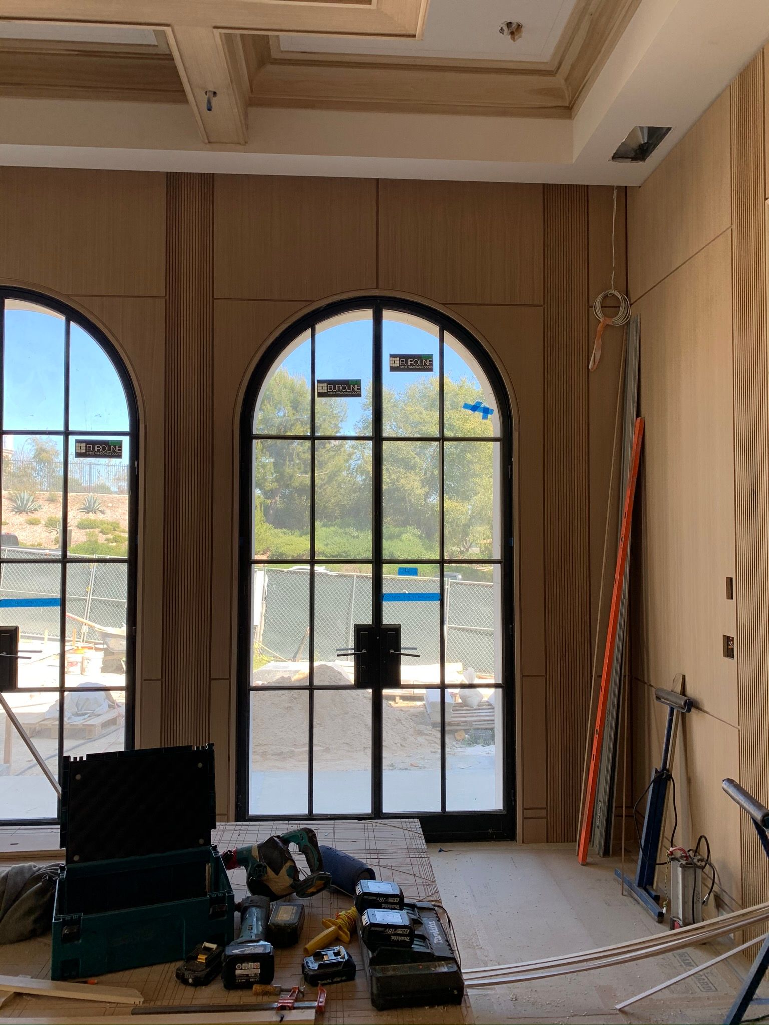 Interior room with arched windows, construction tools on floor, light wood paneling.