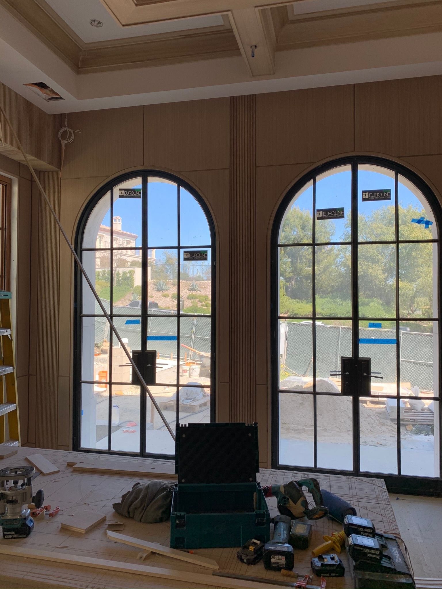 Two arched windows with black frames in a building under construction.