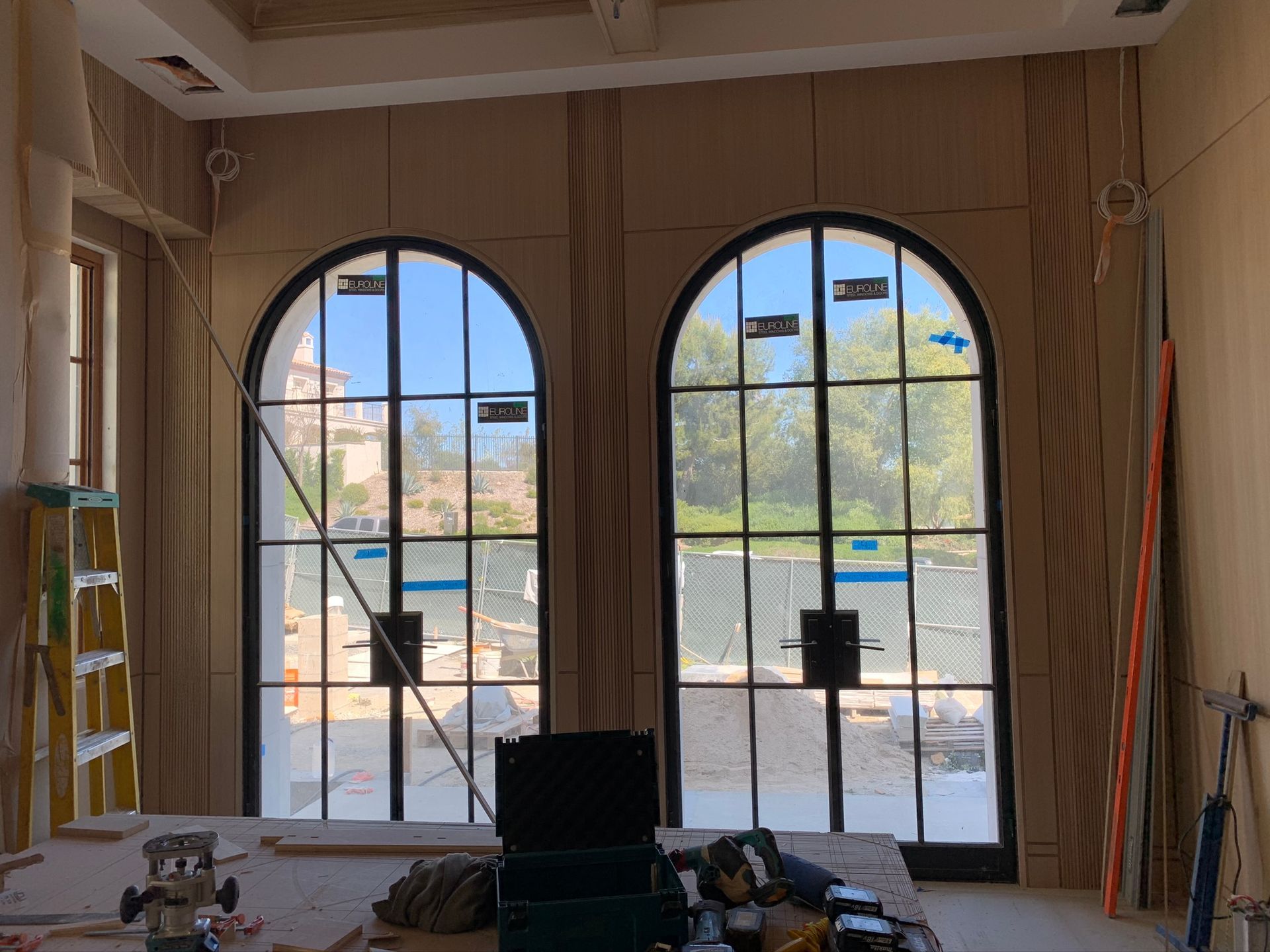 Large arched windows in a room under construction, with tools on a table in front.