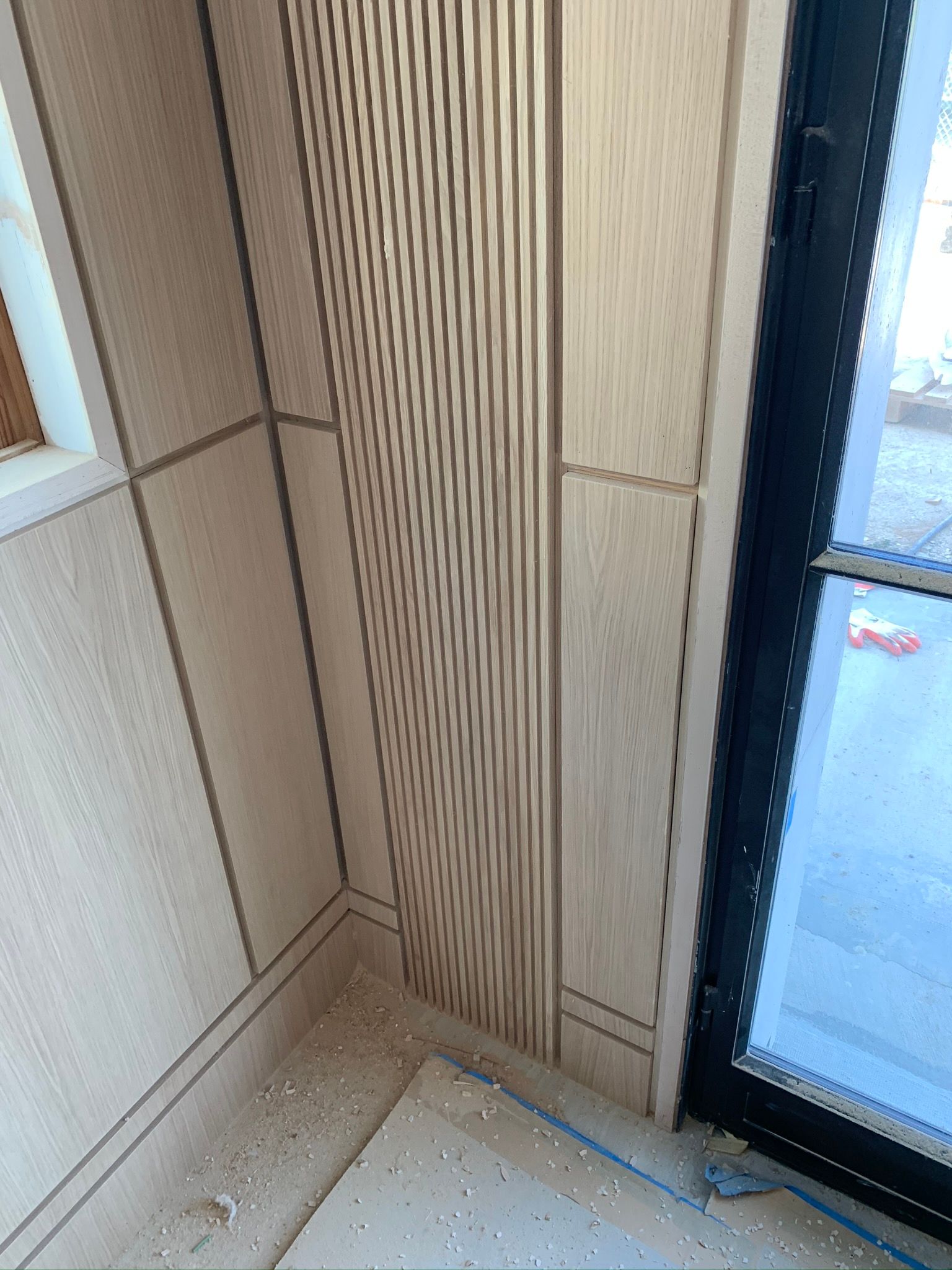 Corner of a room with light wood paneling, including a textured curved section and a window.