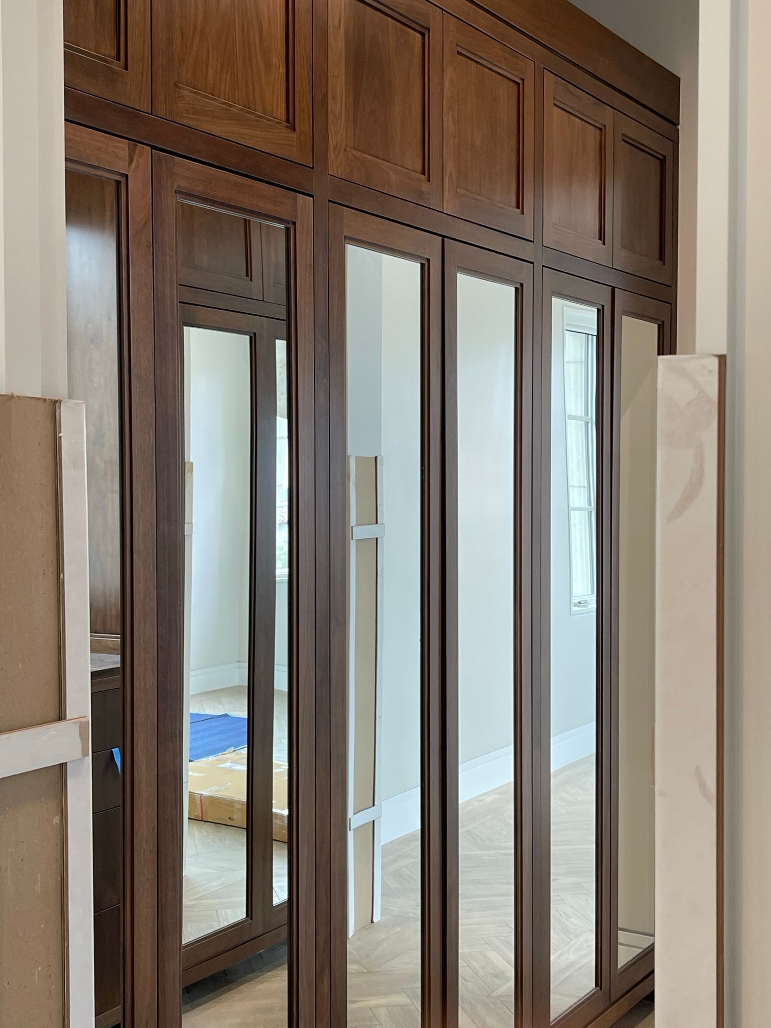 Wooden mirrored closet doors, paneled, in a room. Brown wood, reflective glass.