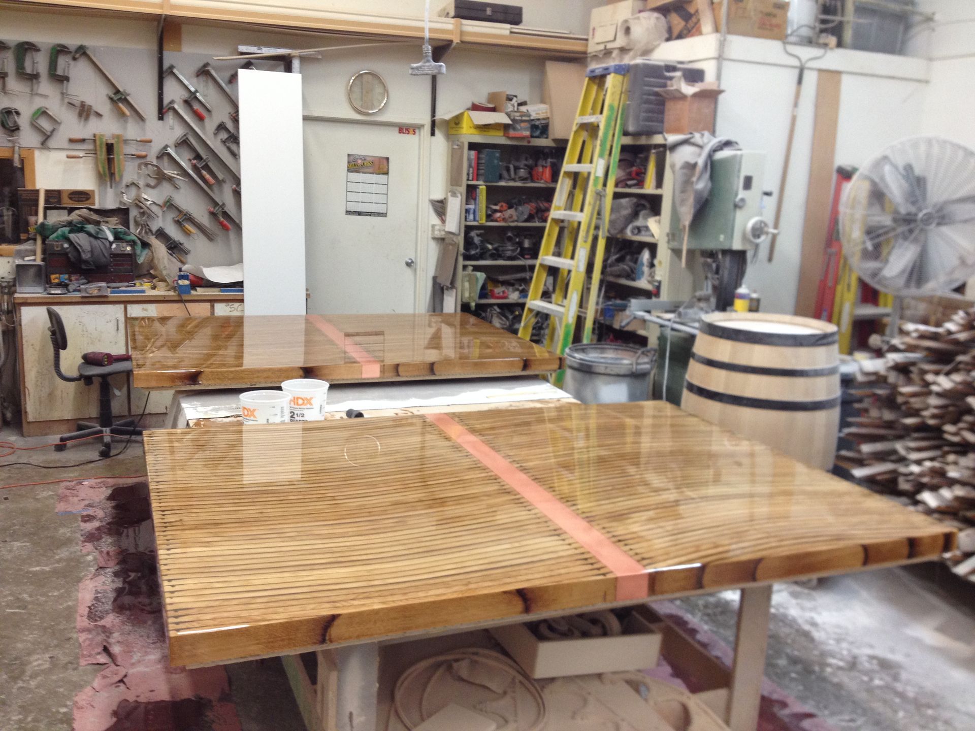 Two wooden tables with glossy finish in a workshop. One has a pink stripe.