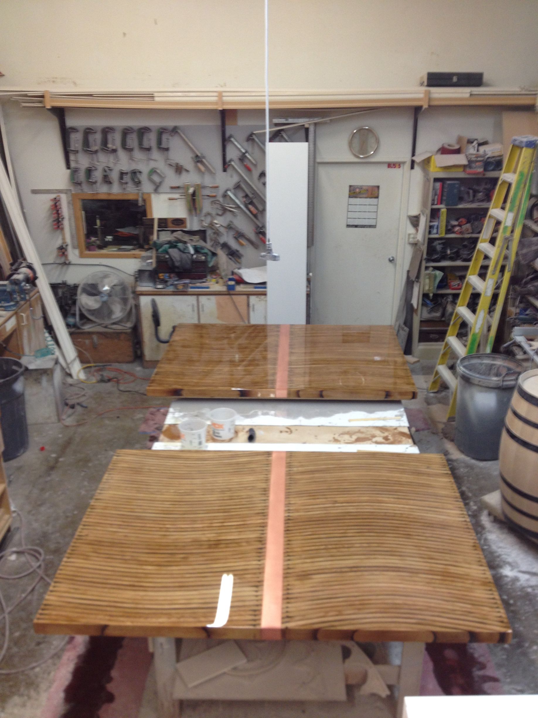 Two wood tabletops with copper strip detail in a workshop, tools on the wall, ladder.