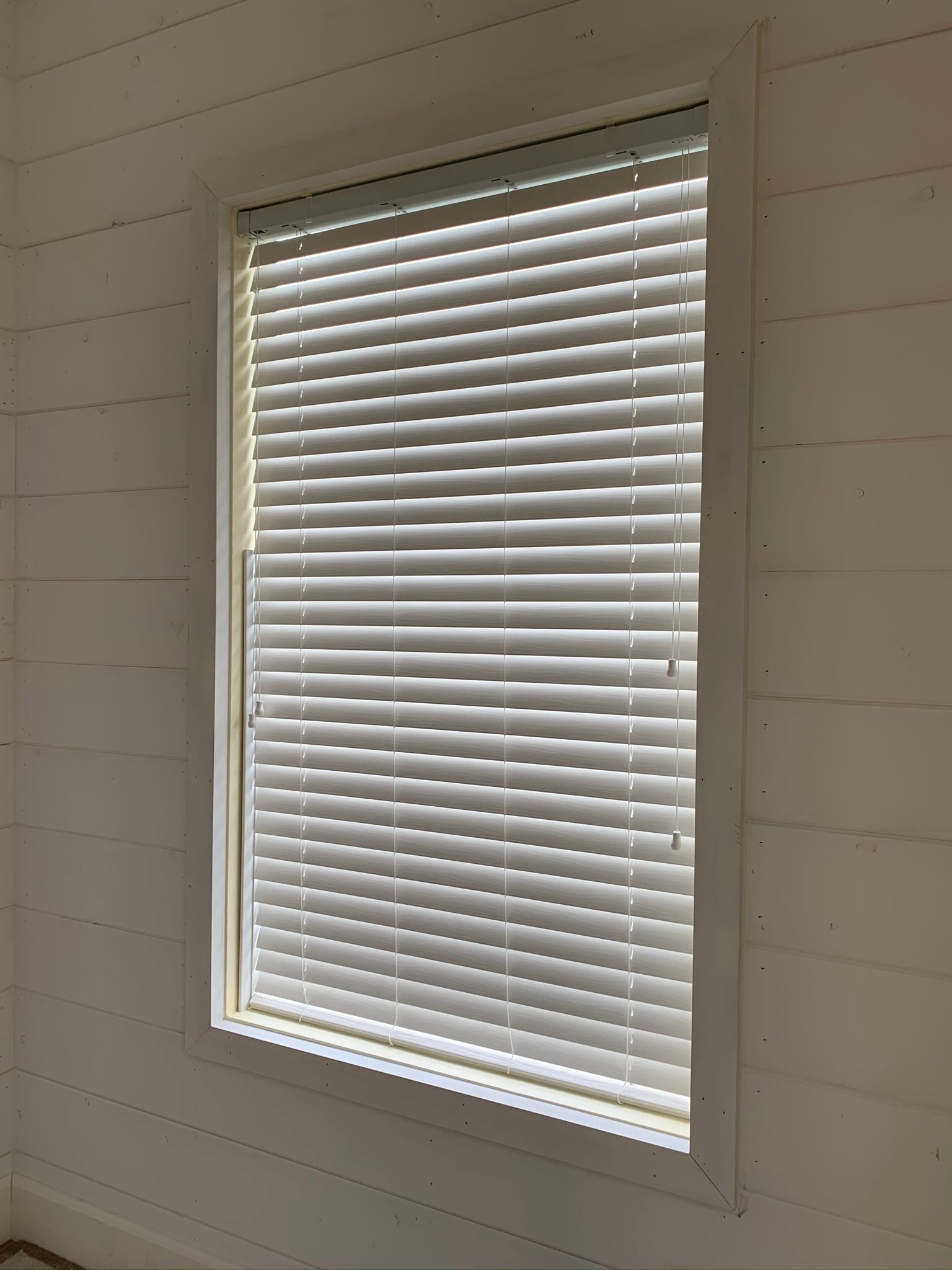 White window with closed horizontal blinds in a white-paneled room.