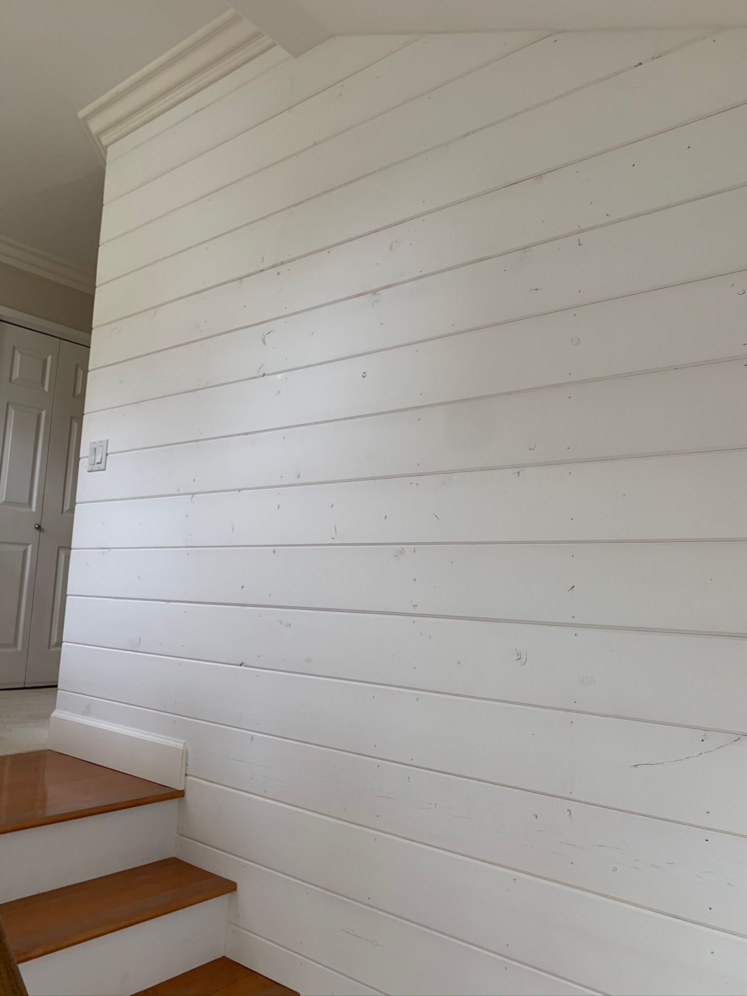 White plank wall next to wooden staircase with white door visible.