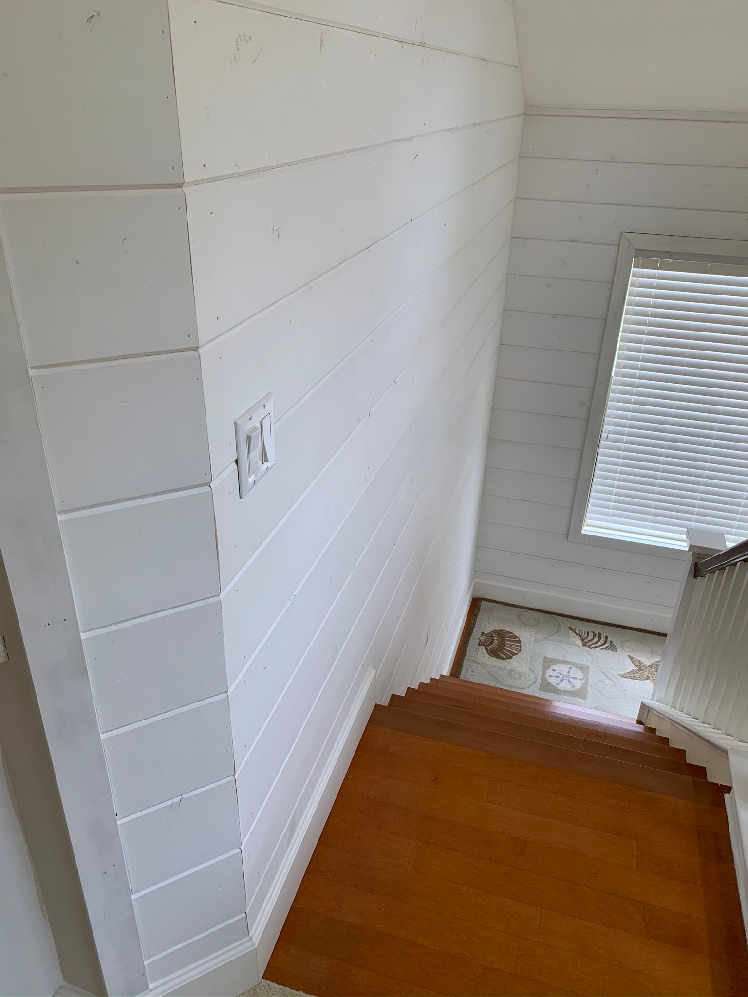 White shiplap wall alongside wooden stairs and a window with blinds.