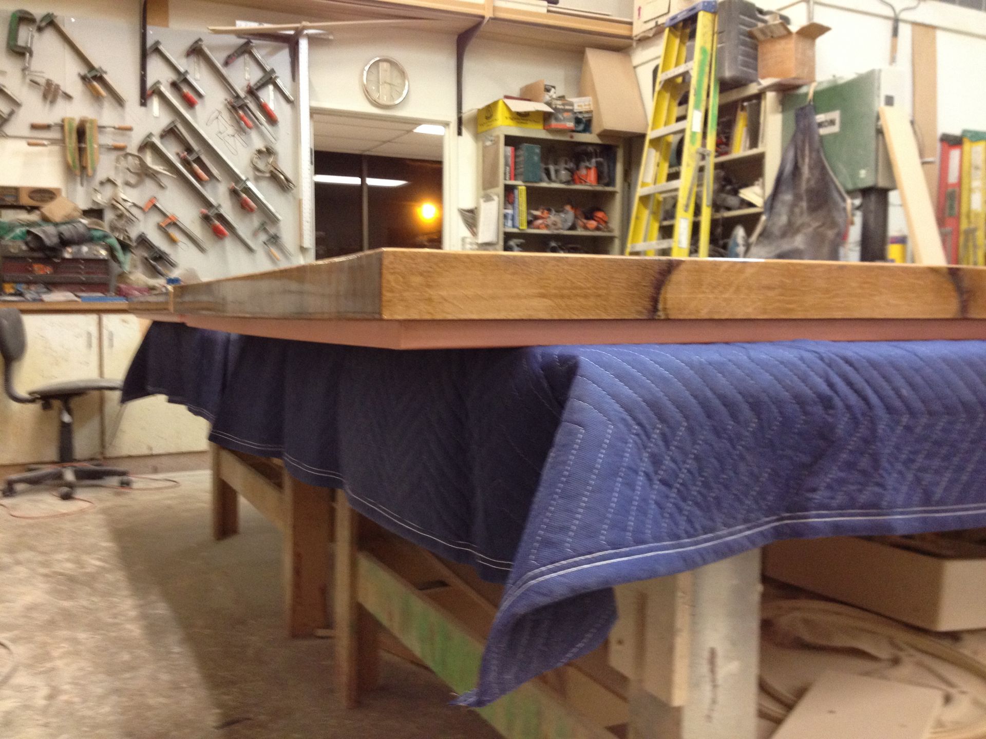 Wooden workbench with a large plank and blue quilted cover in a workshop.