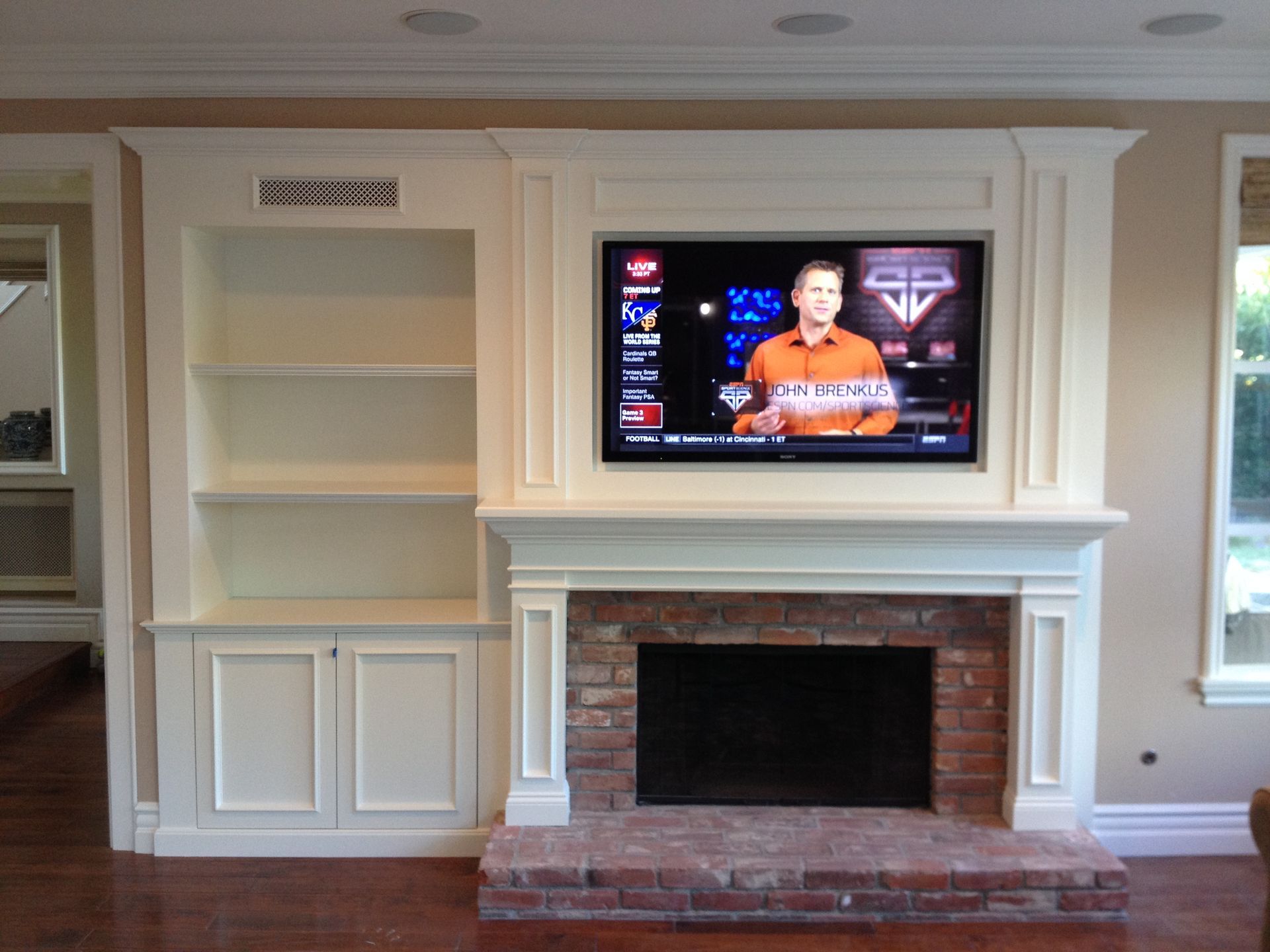 Built-in white entertainment center with fireplace, TV, and shelves. Man reporting news on screen.