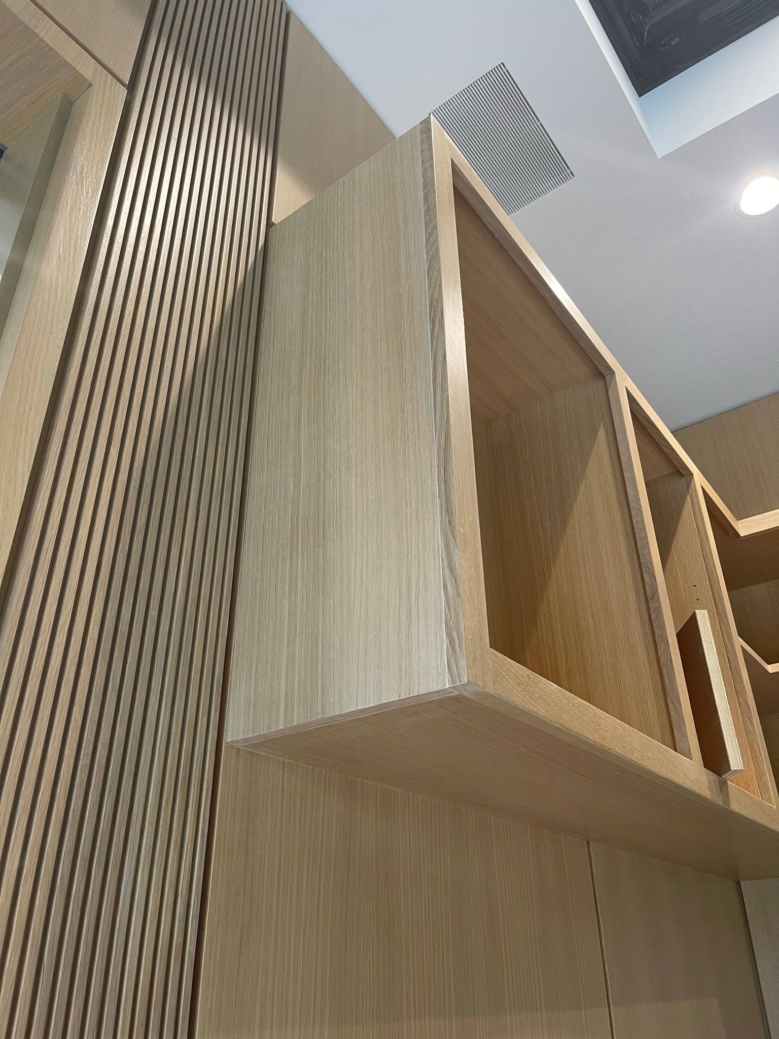 Built-in wooden cabinetry with open shelves and a textured vertical panel. Warm, neutral tones.
