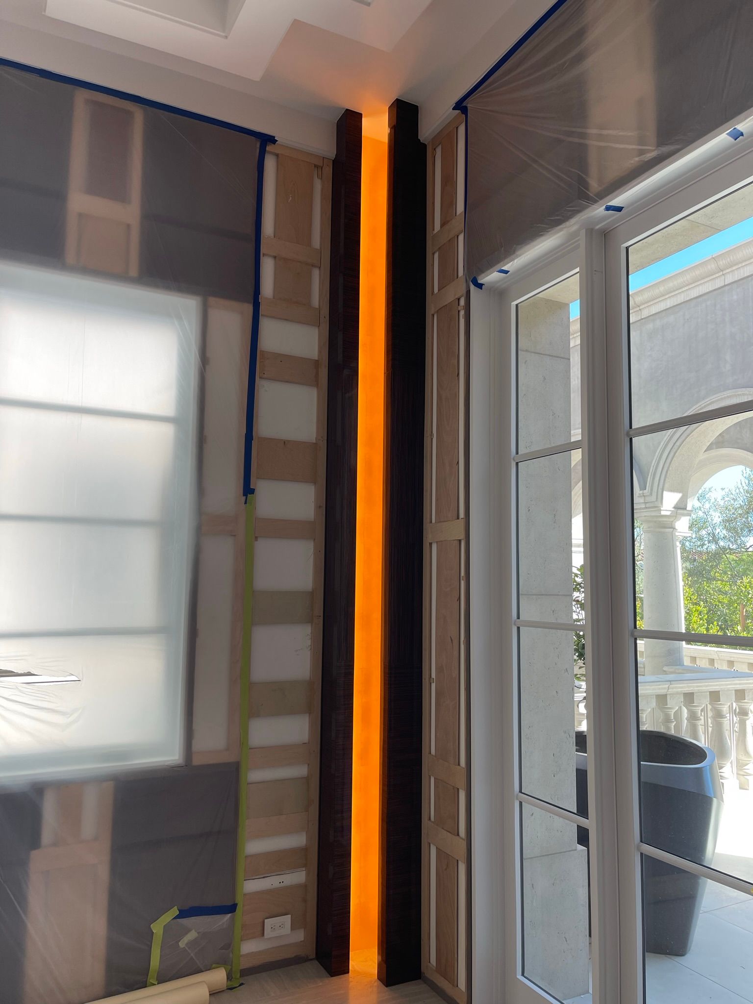 Vertical dark wooden beam with amber lighting between panels, next to a glass door.