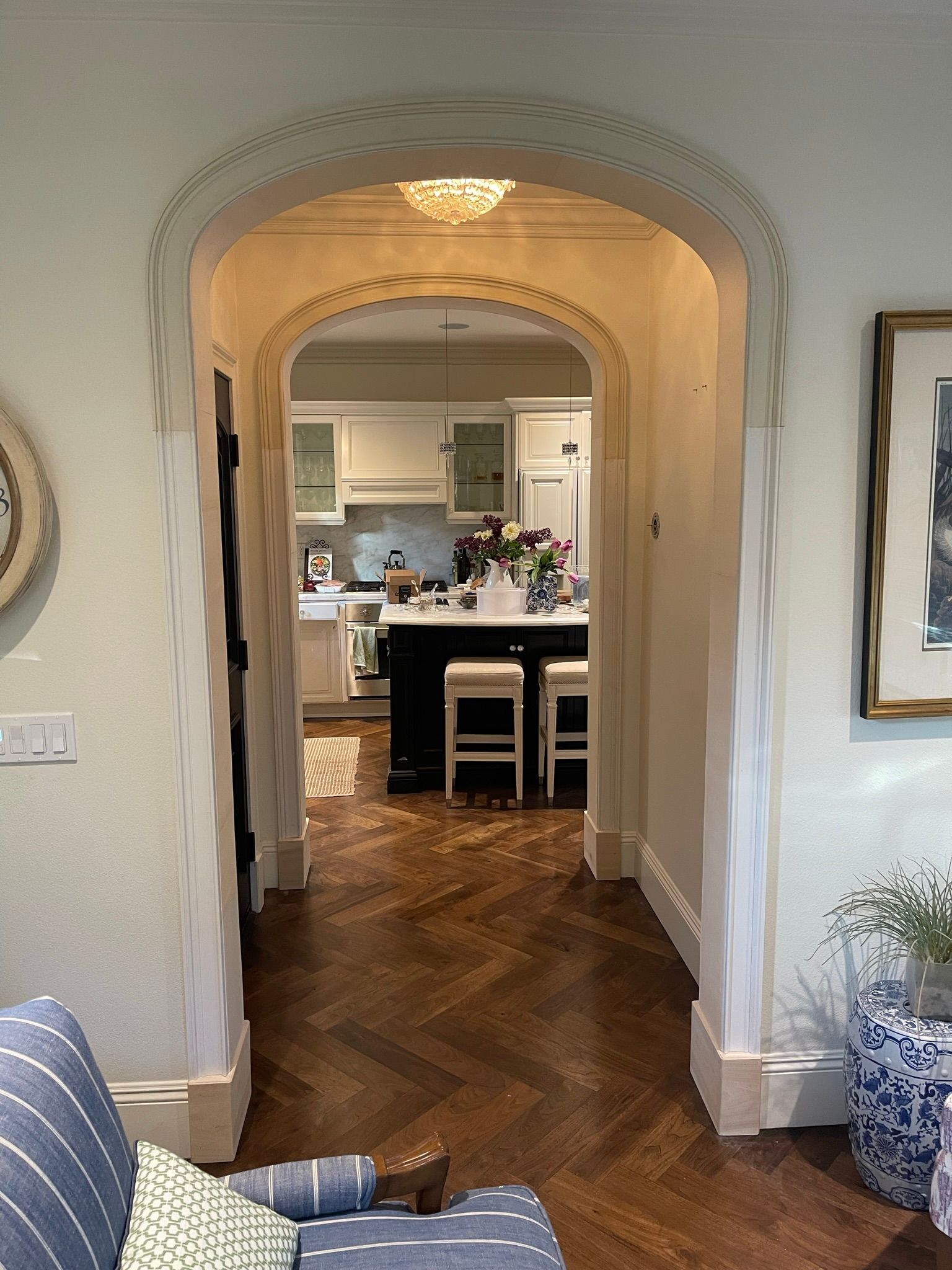 Archway opening to kitchen with dark wood floor, white cabinets, and island.