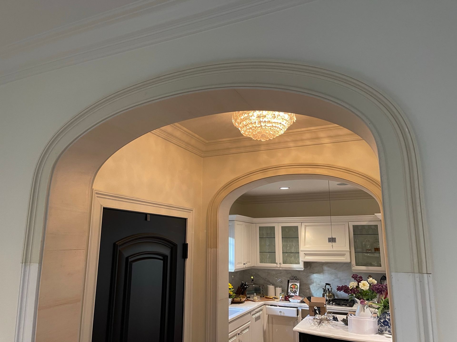 Arched doorway with decorative trim, revealing a kitchen and a black door.