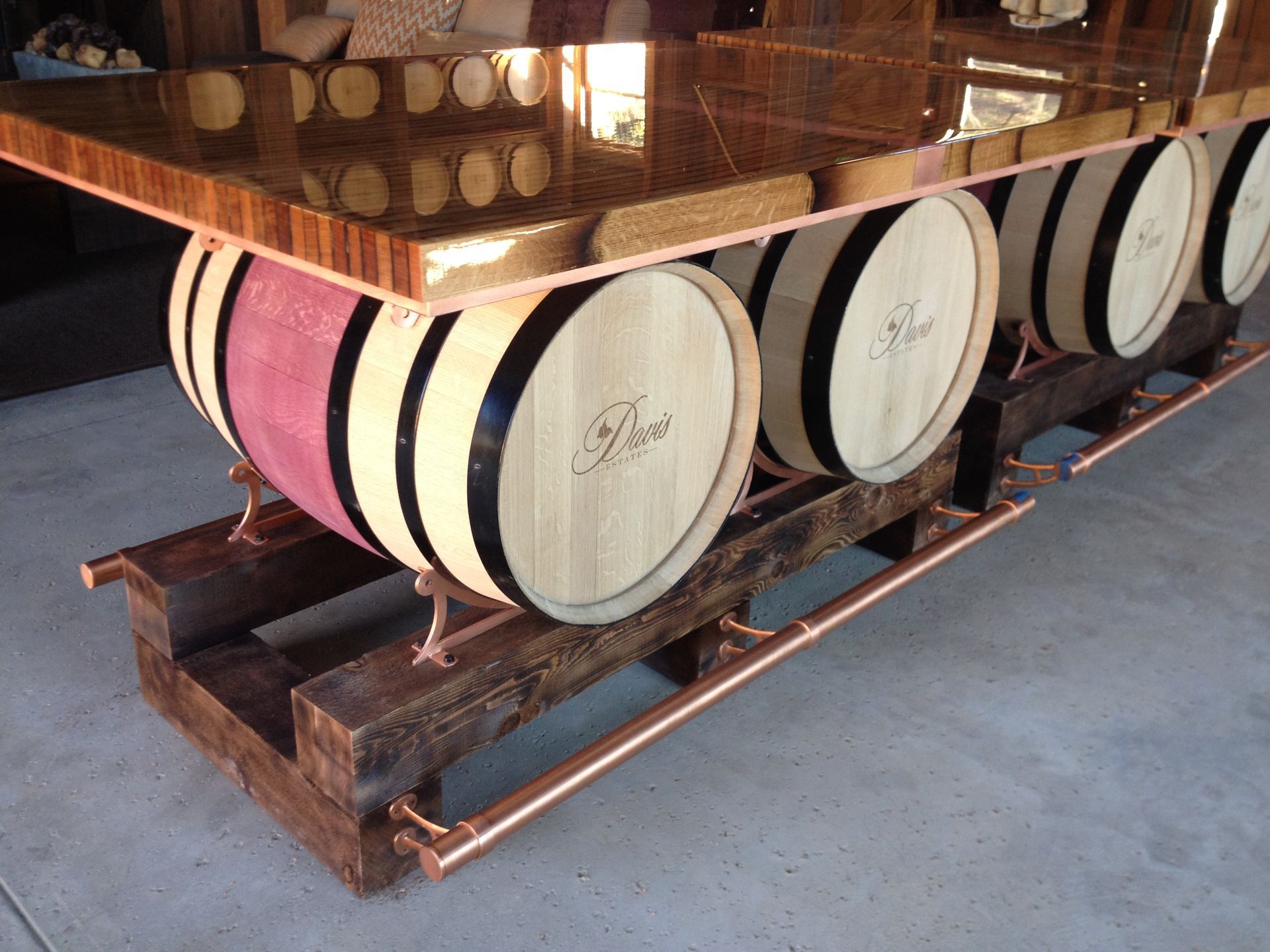 Bar with wooden top supported by wine barrels and a copper pipe frame.