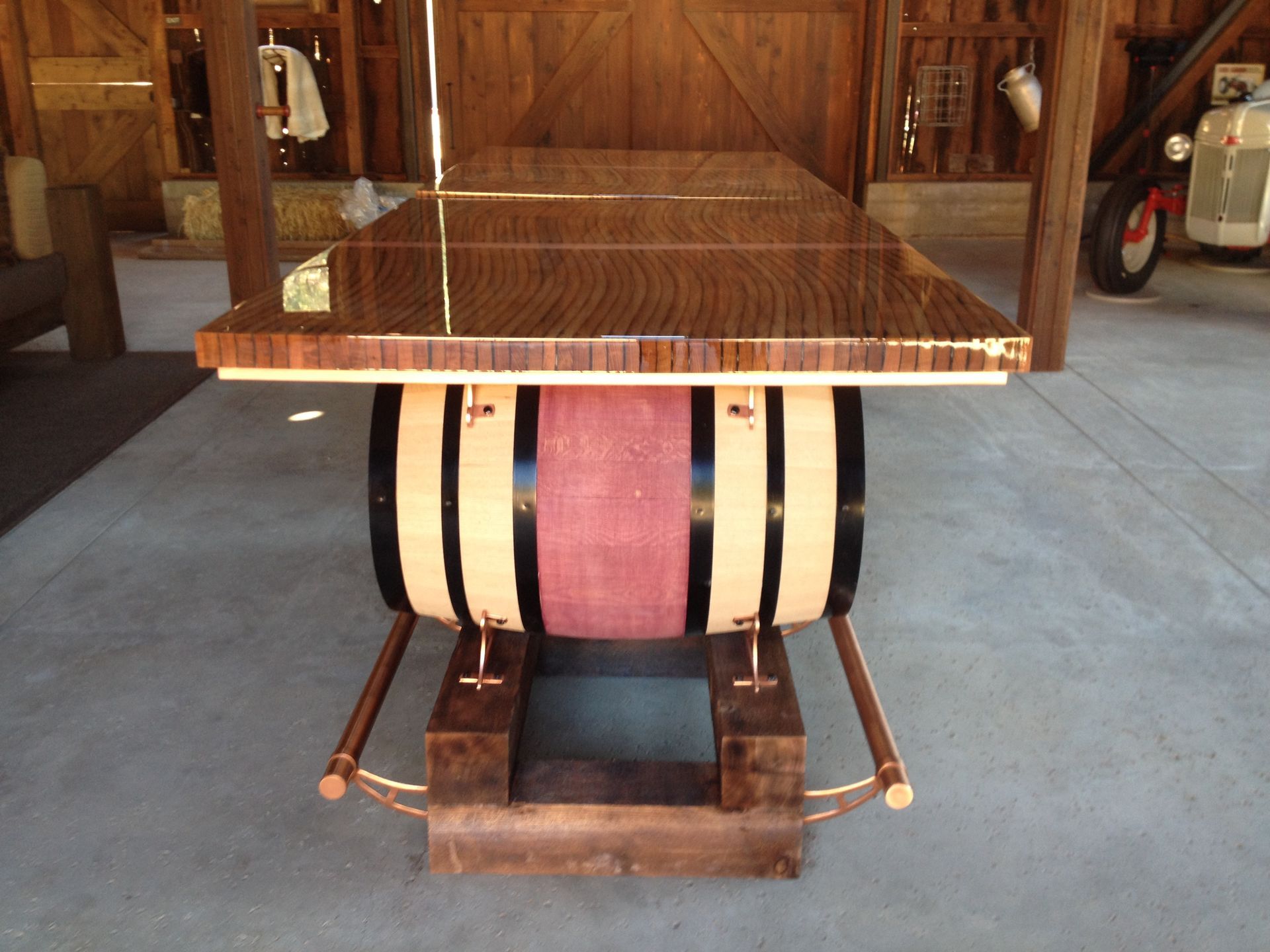 A wooden table with a barrel base, in a barn setting, with a tractor visible.