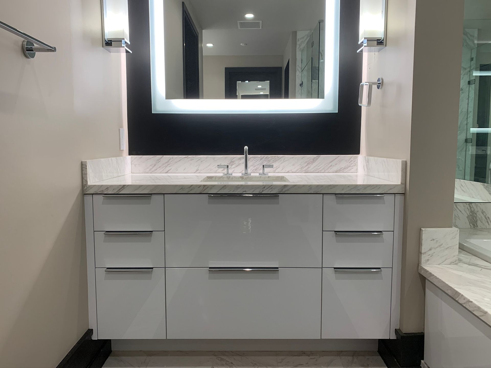 Modern white bathroom vanity with illuminated mirror and chrome fixtures.