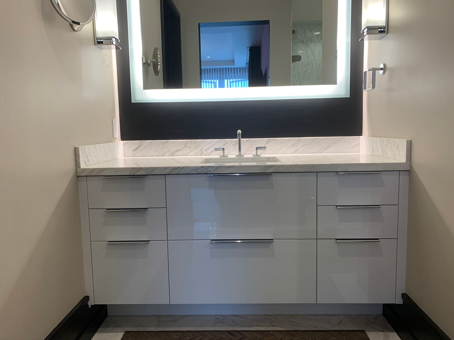 Modern white bathroom vanity with illuminated mirror, countertop, and drawers.