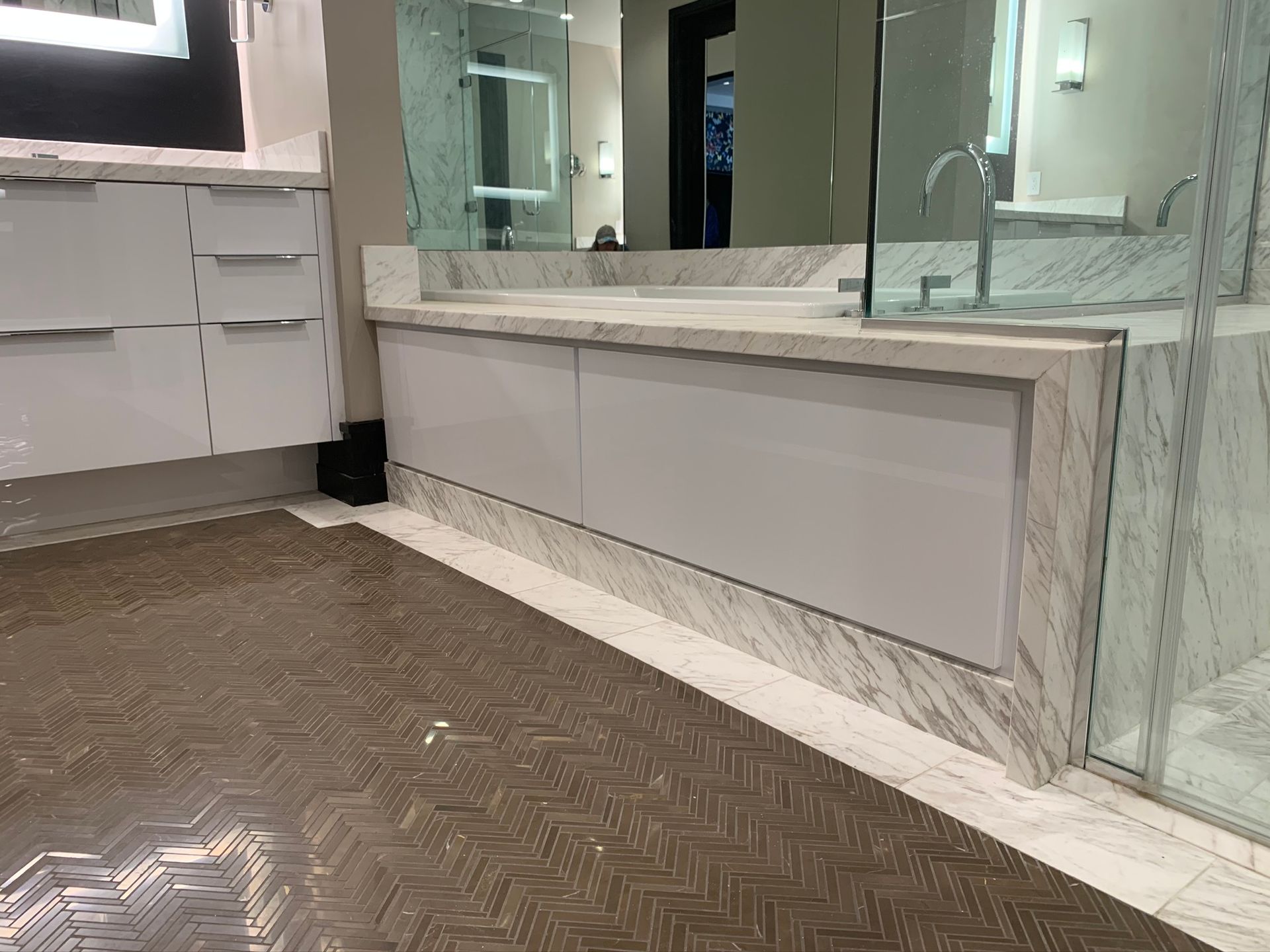 Modern bathroom with white cabinets, marble counters, and patterned tile floor.
