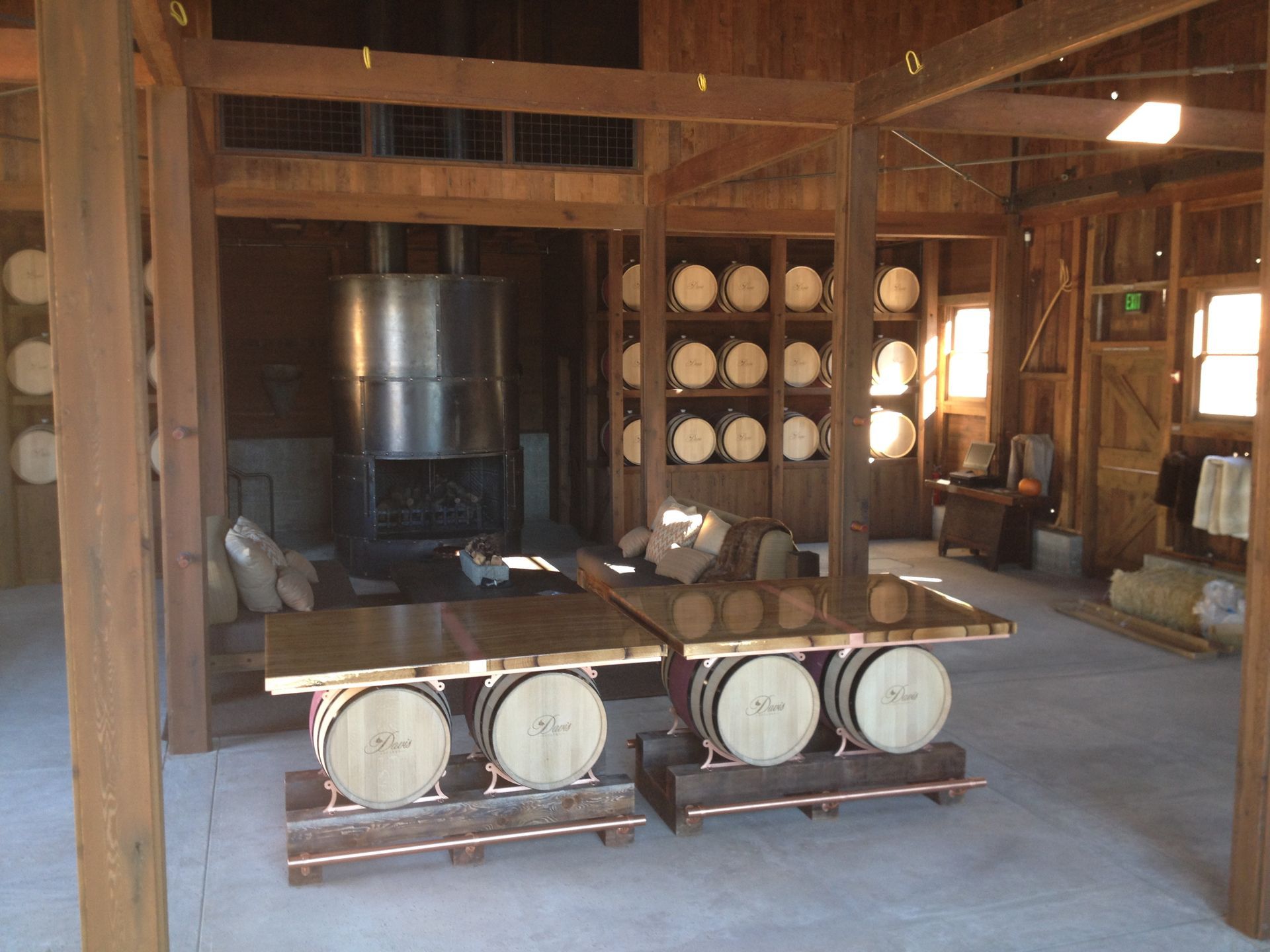 Two tables made of barrels in a rustic wooden room. Barrels stacked on shelves. Metal still.