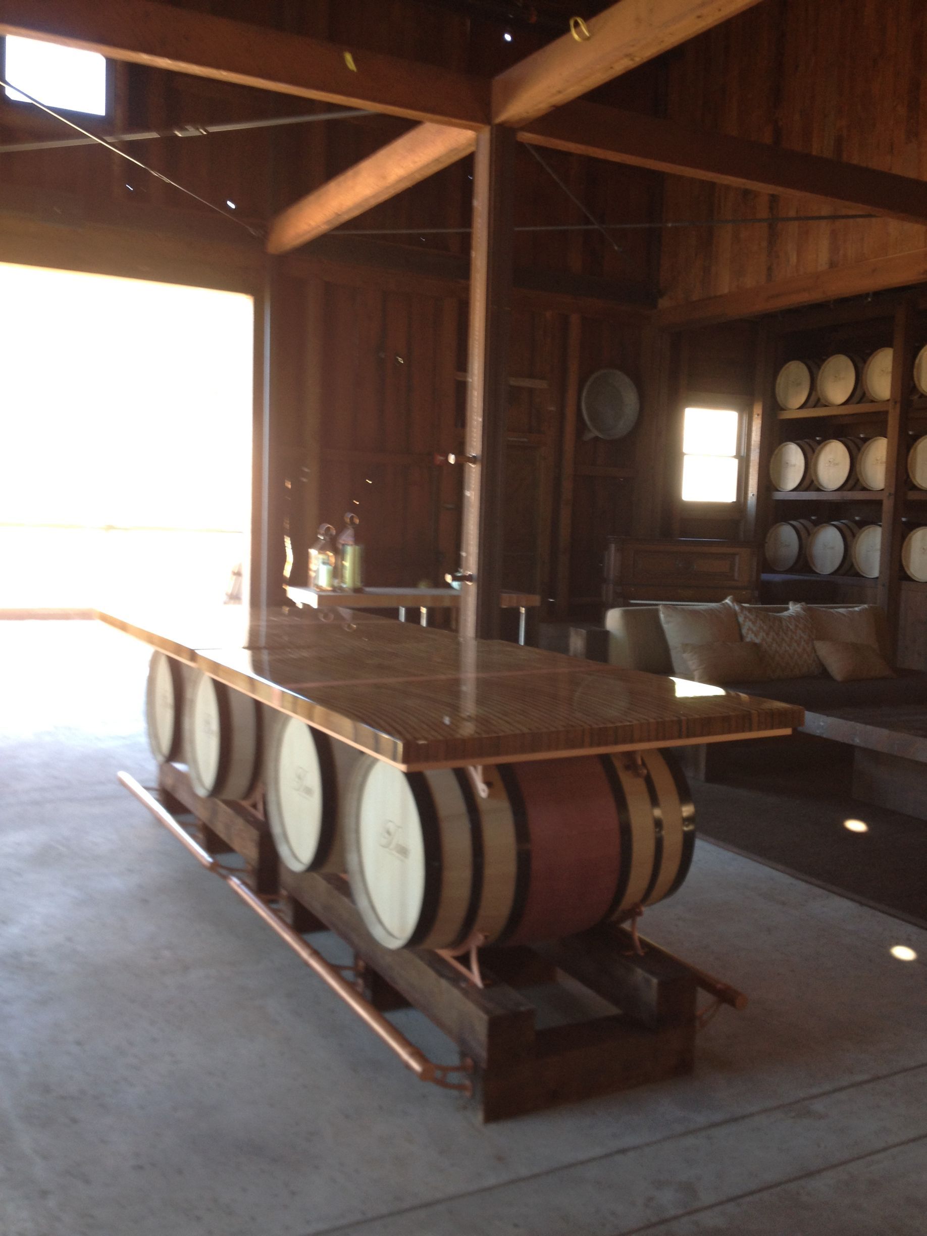 Bar constructed from wine barrels, wood, and copper, inside a wooden building with open entrance.