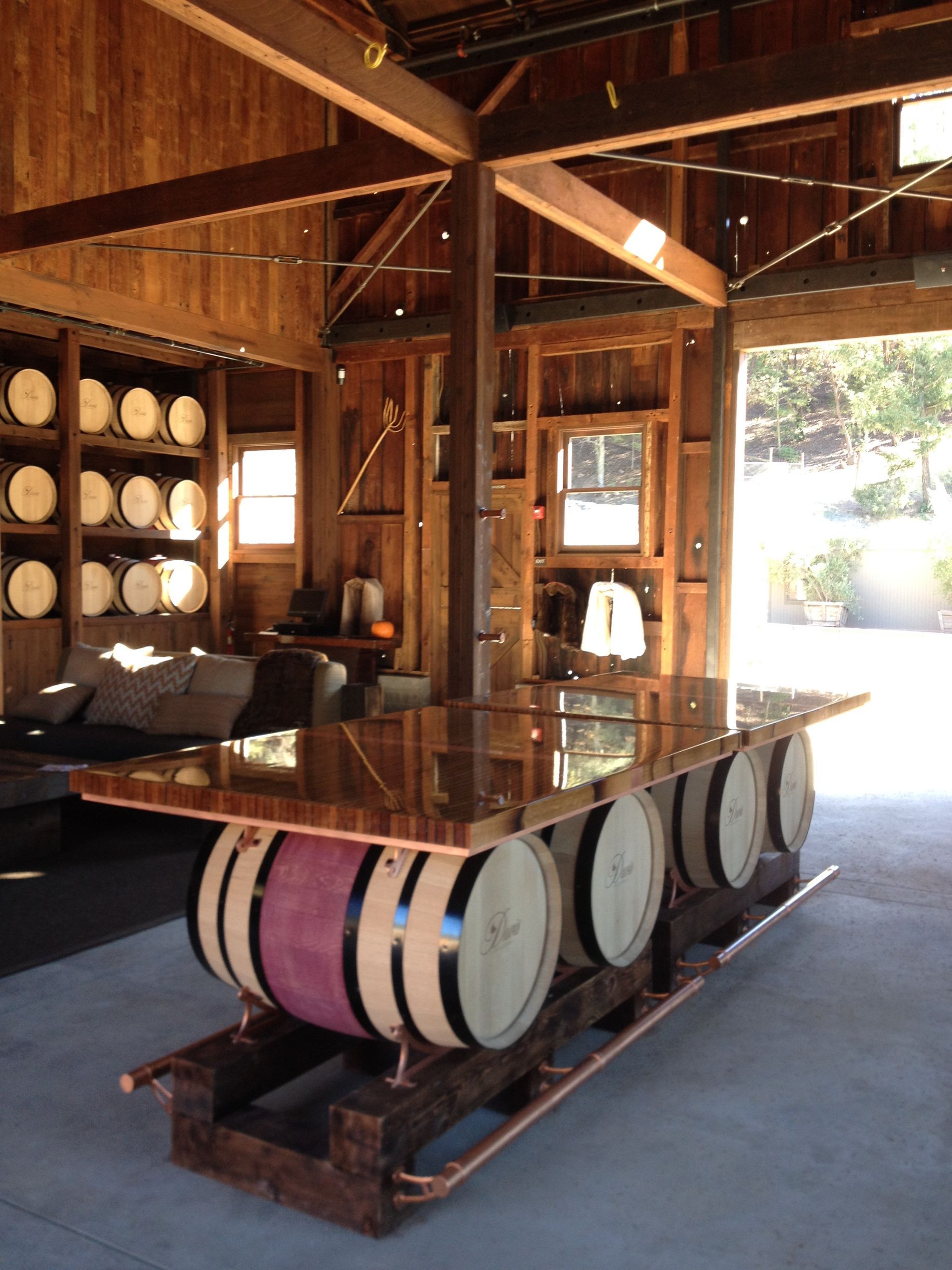 A wooden bar built from barrels, with copper top, inside a wooden building with barrels on shelves.