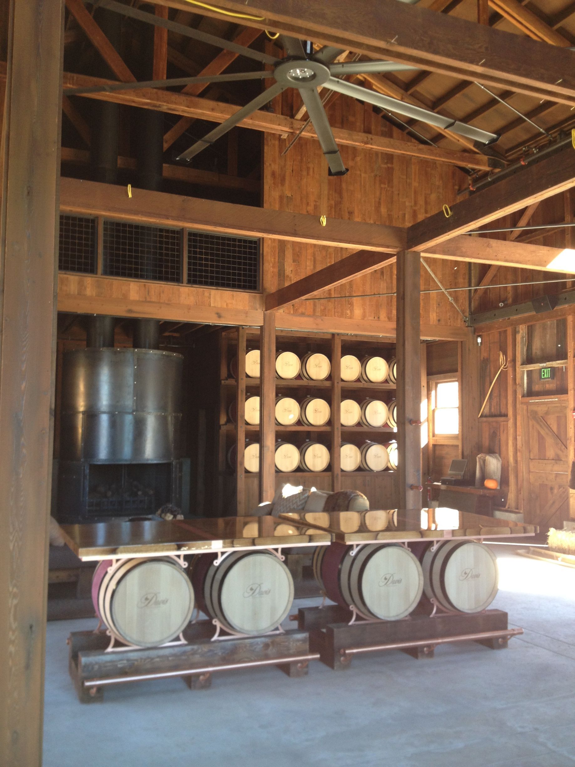 Interior of a barn with wooden structure, wine barrels, and a large metal still.