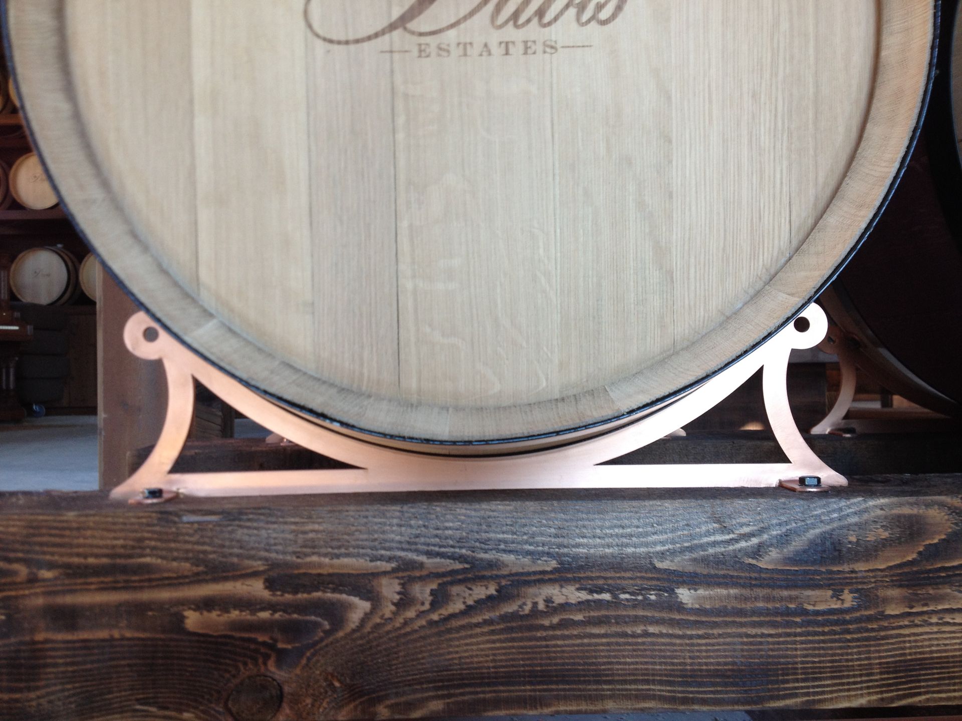 Copper barrel stand holding wooden wine barrel on a wooden surface.