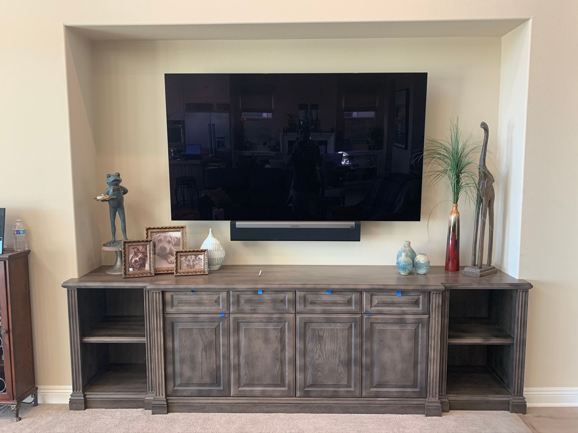 TV mounted above a dark gray cabinet. Decorations on the cabinet include statues, vases, and framed photos.
